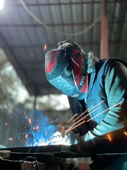 Welder in a red helmet, sparks flying, blue welding light.