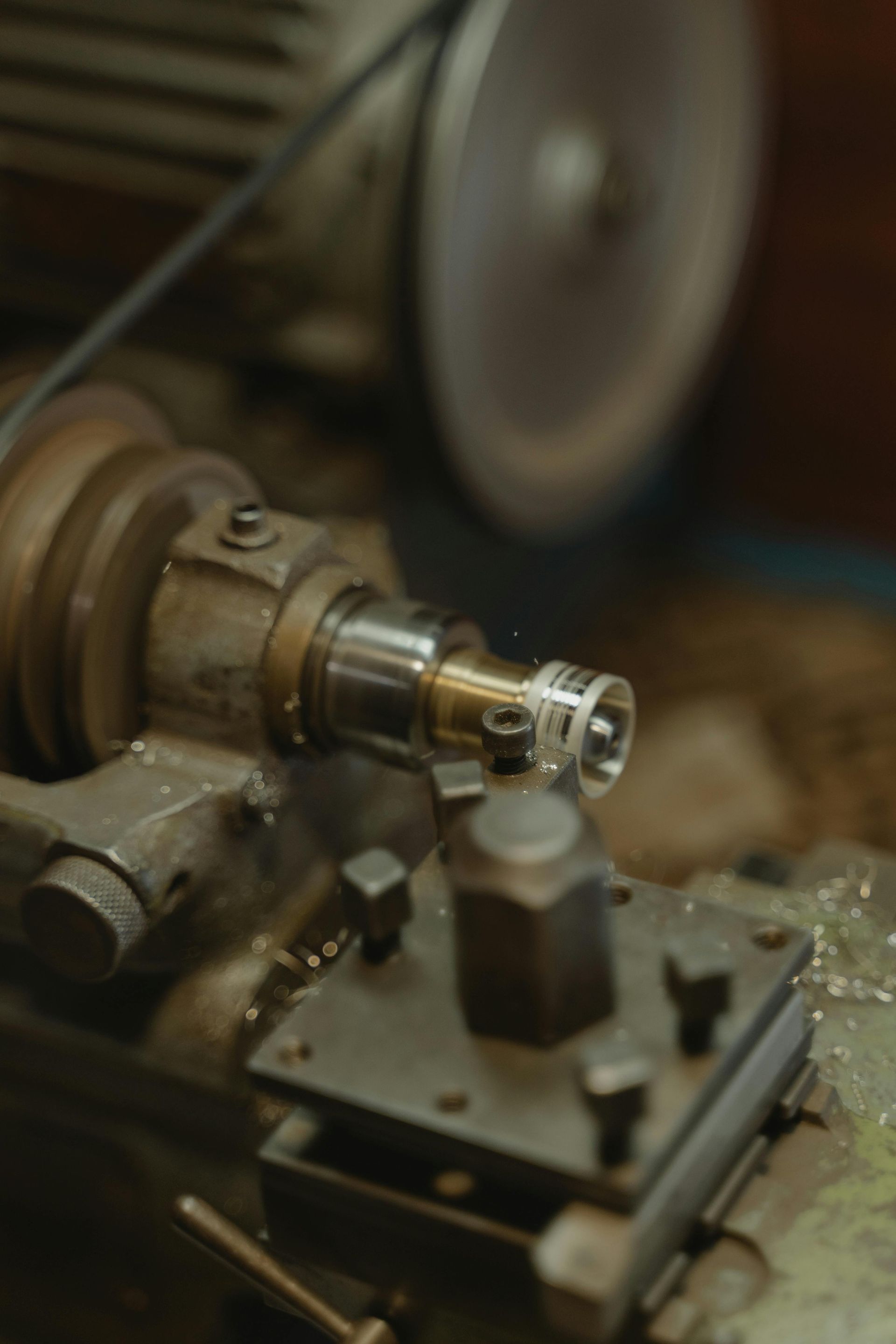 Lathe machine shaping metal piece, close-up. Focus on spinning metal with shavings, grey and metallic tones.
