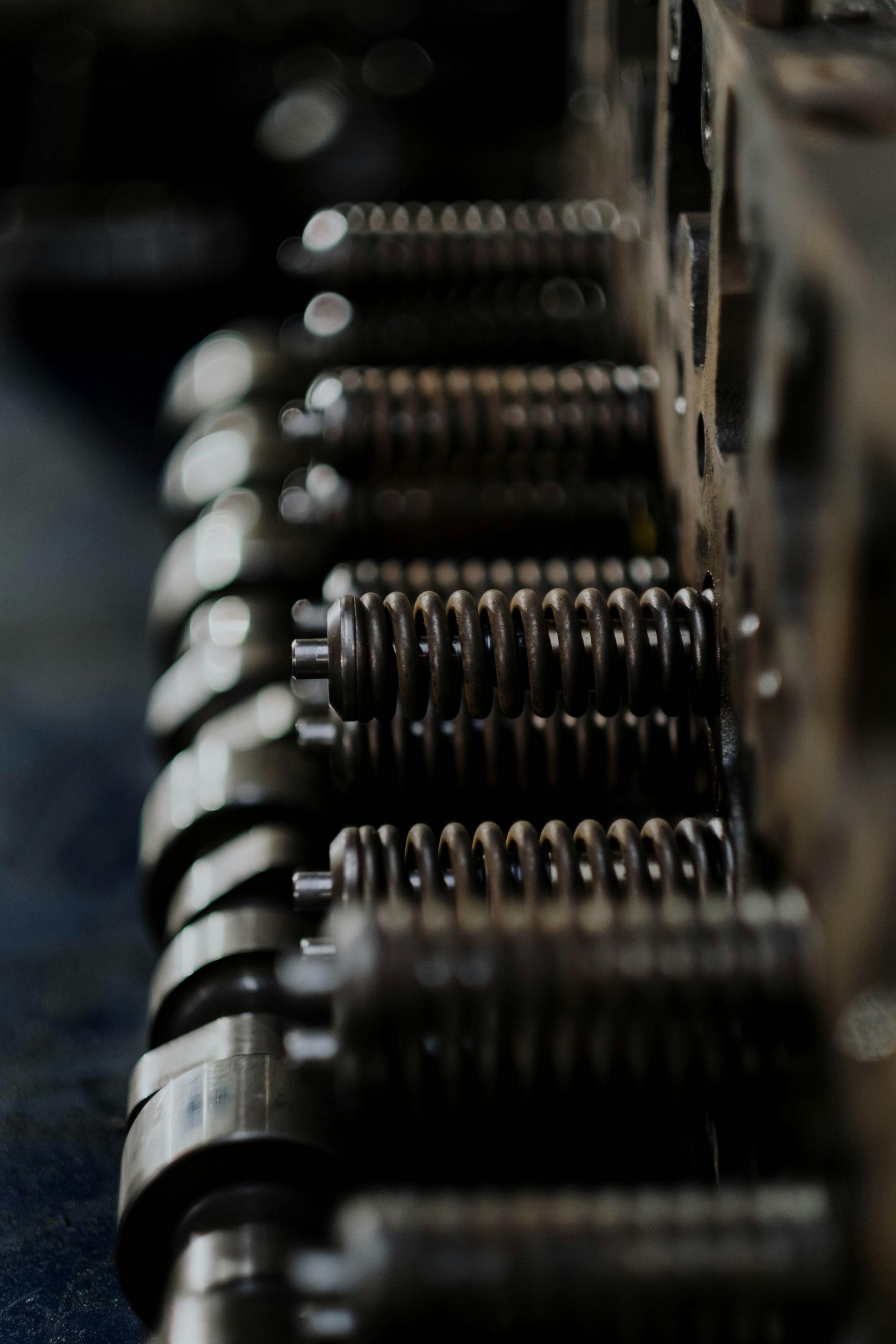 Close-up of engine valve springs and components, metallic silver against a blurred dark background.