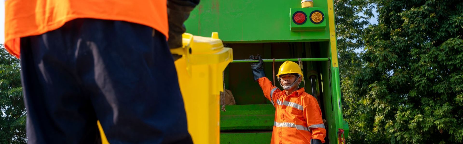 A man in an orange vest is standing next to a garbage truck.