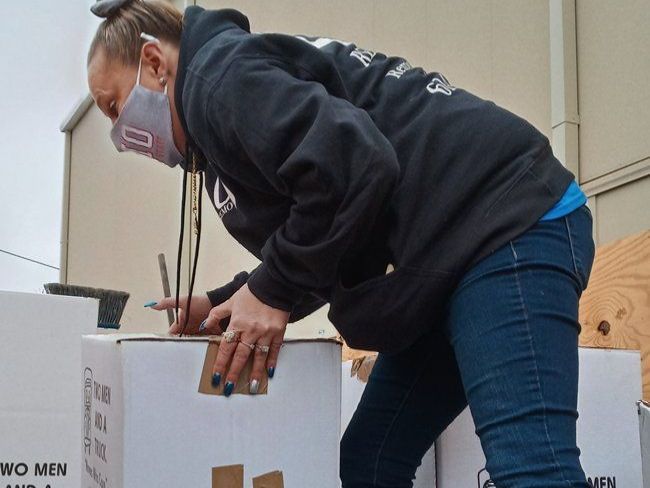 A woman wearing a mask is bending over to pick up a box