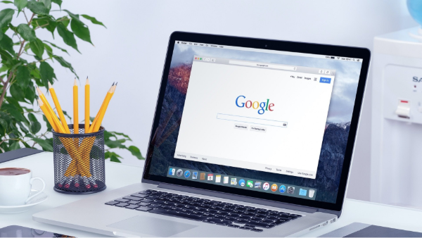 Laptop displaying Google homepage on a desk next to pencils, a plant, and a cup of coffee.