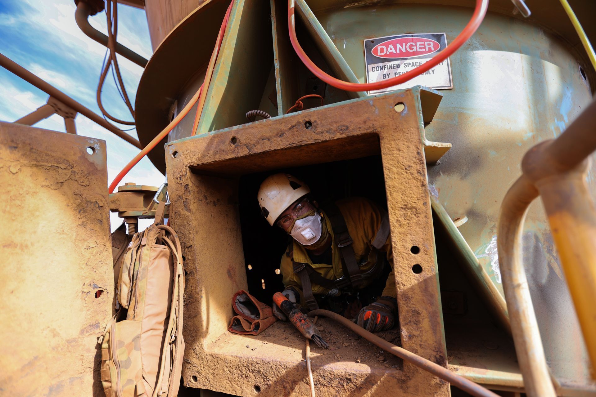 Worker inside industrial equipment, wearing protective gear, welding.