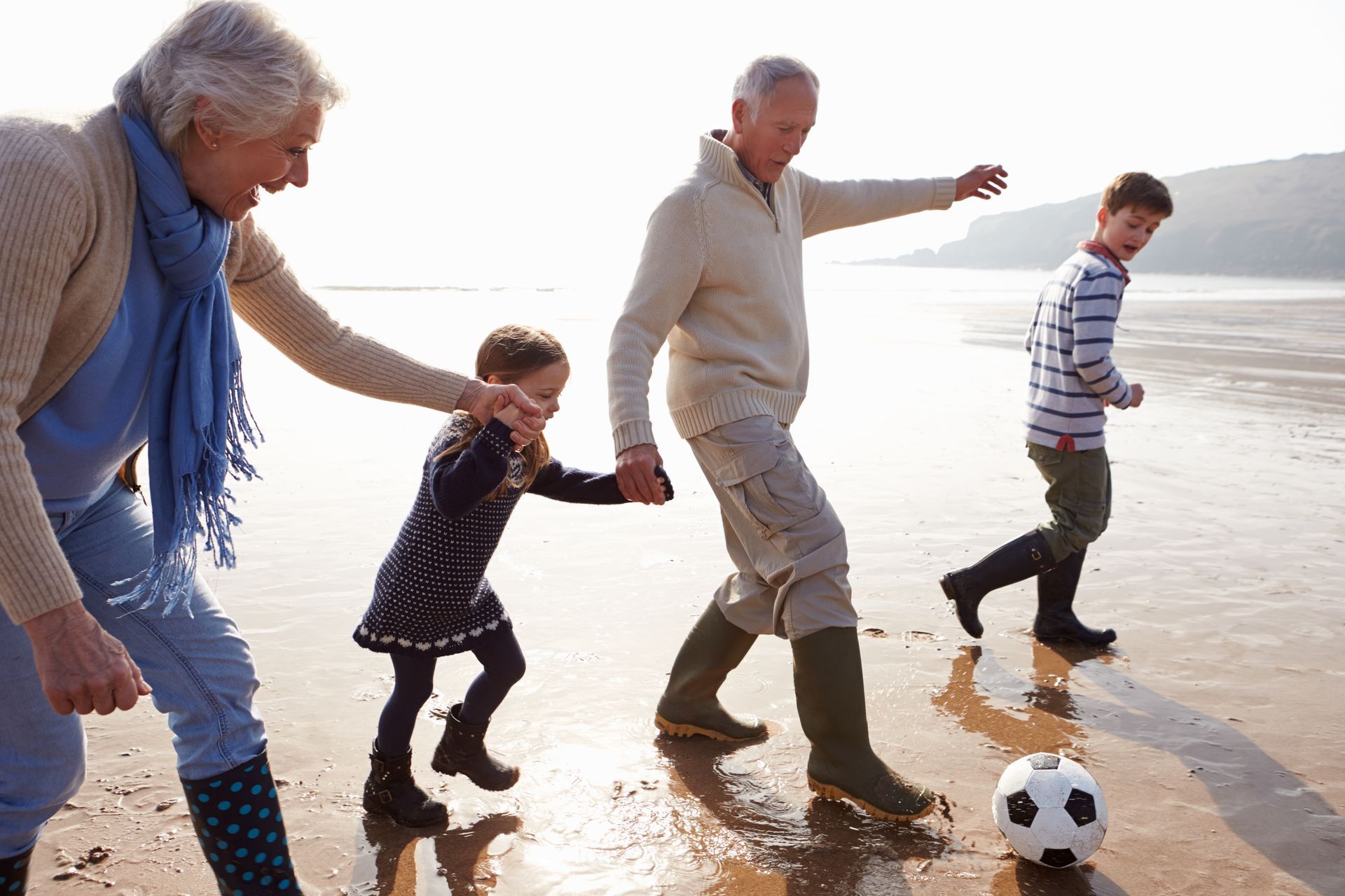 a family is playing with a soccer ball on the beach .