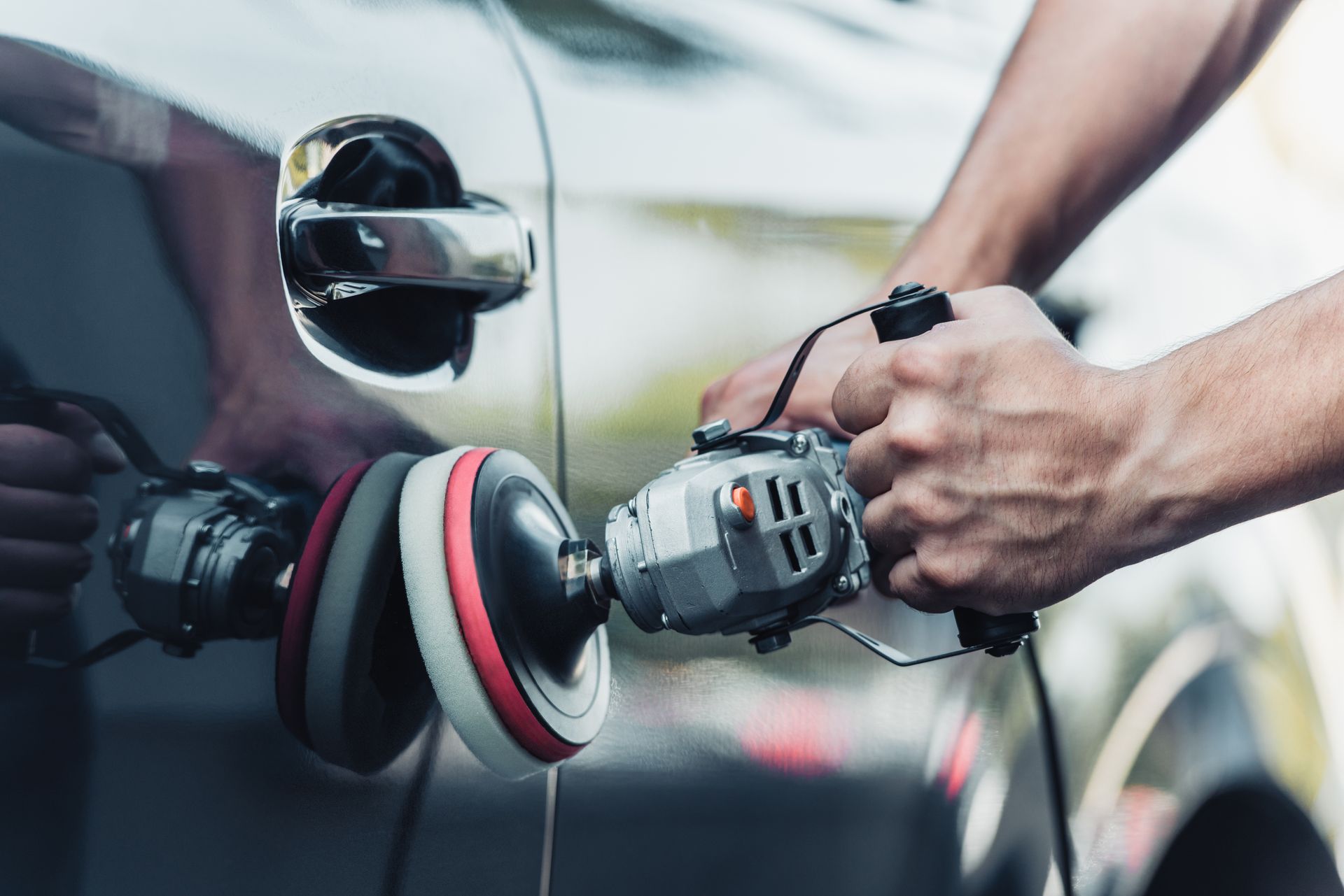 Person polishing a car door with an electric buffer; close-up view.