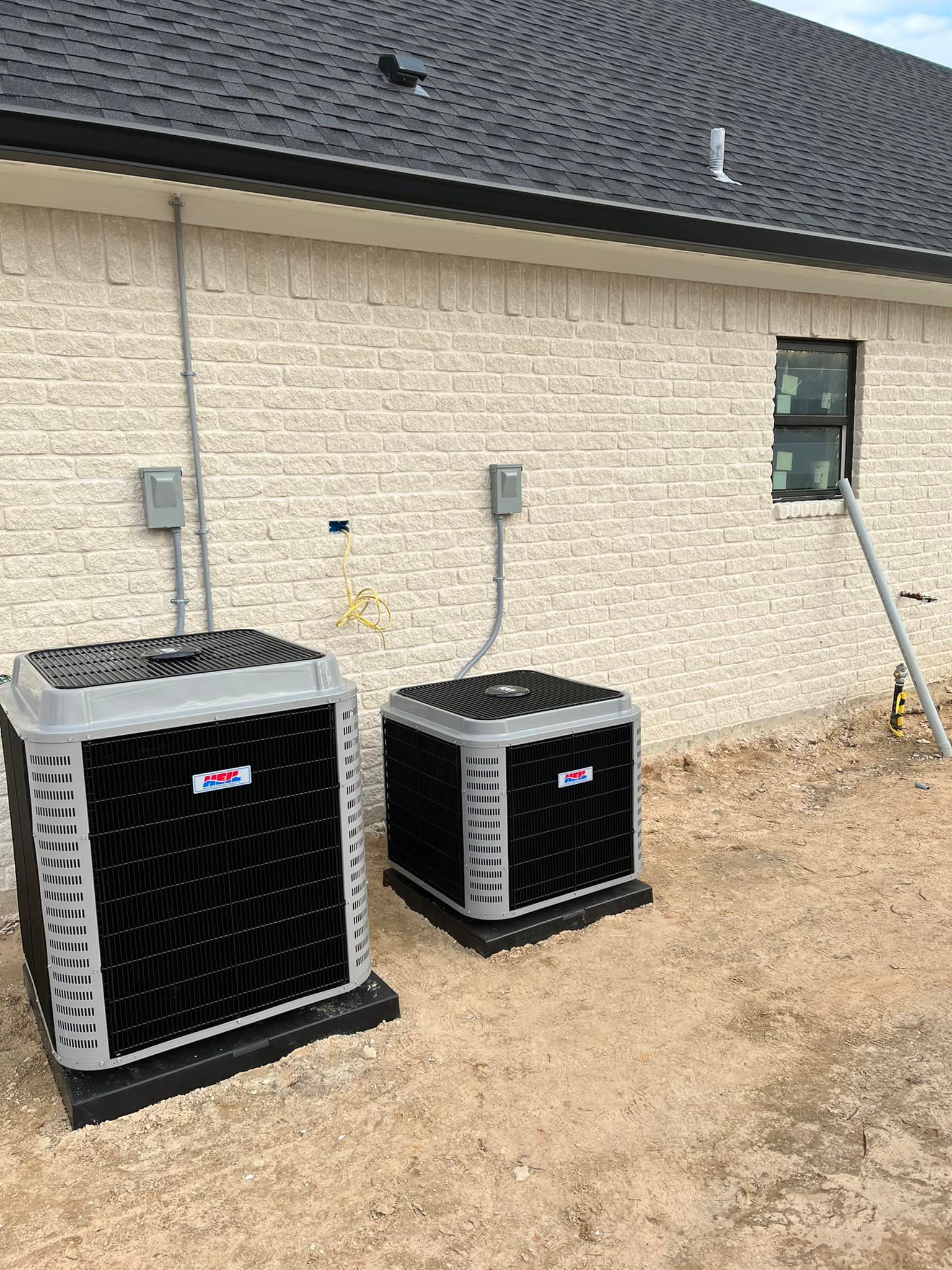 Two air conditioners are sitting outside of a brick building.