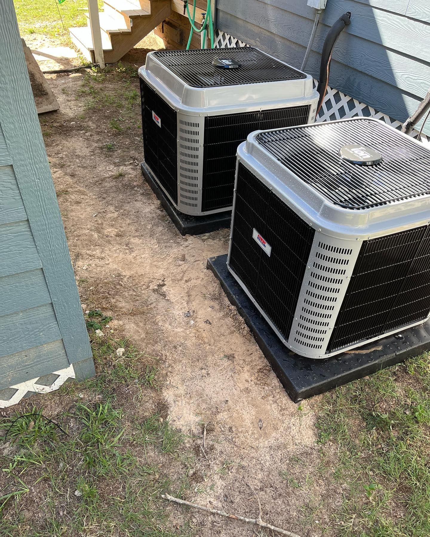 Two air conditioners are sitting on the ground in front of a house.