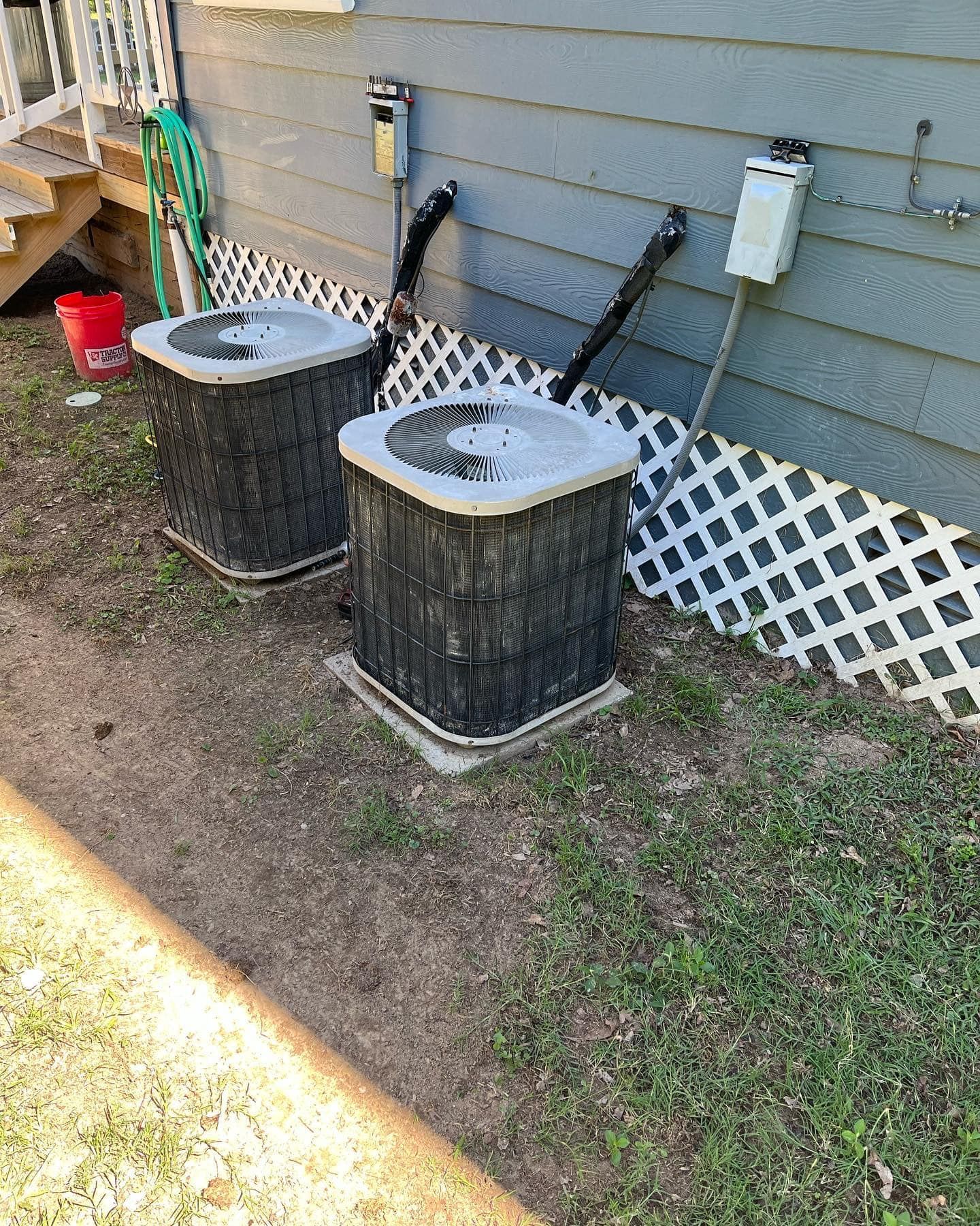 Two air conditioners are sitting next to each other on the side of a house.