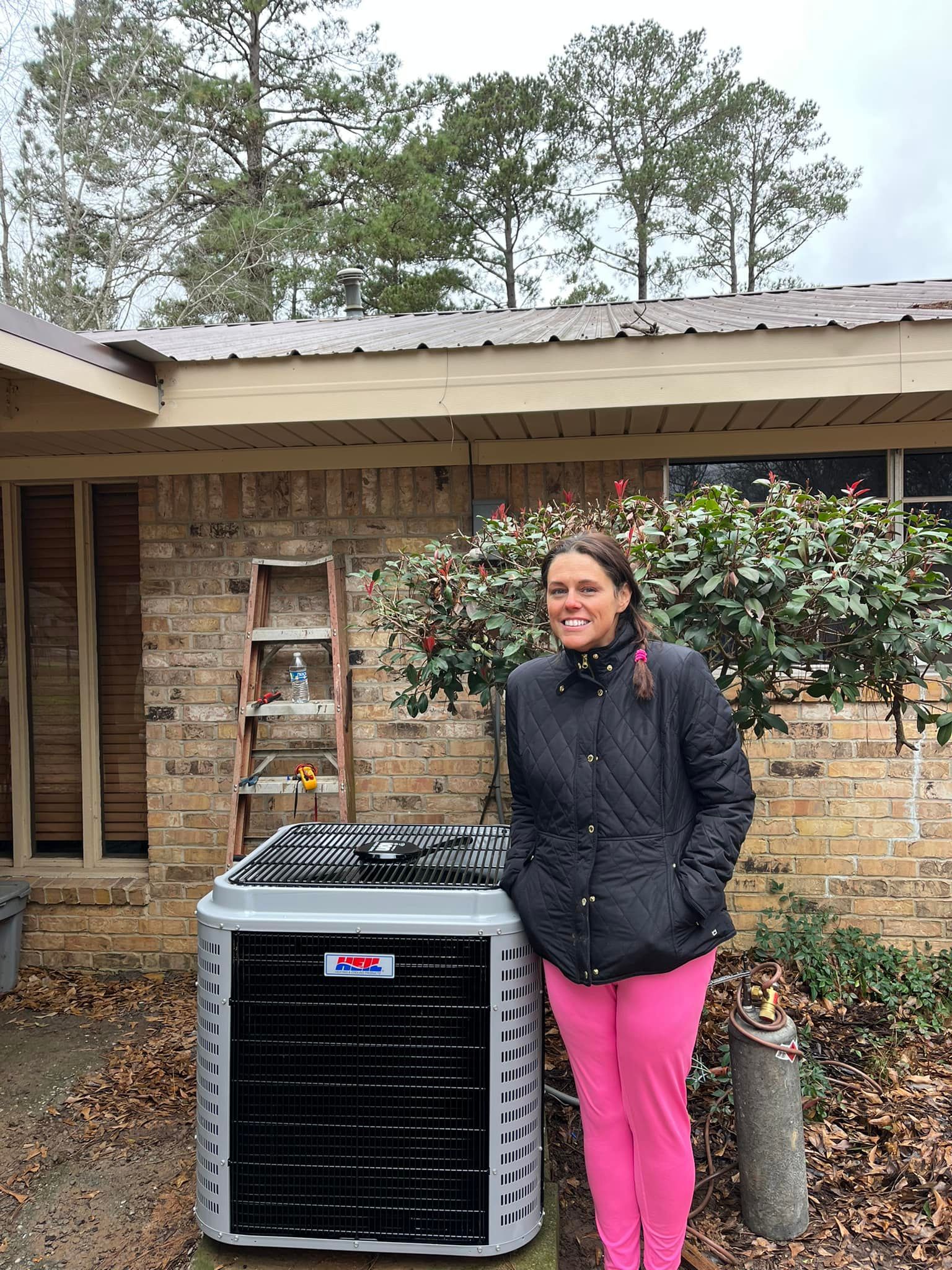 A woman is standing in front of a house next to an air conditioner.