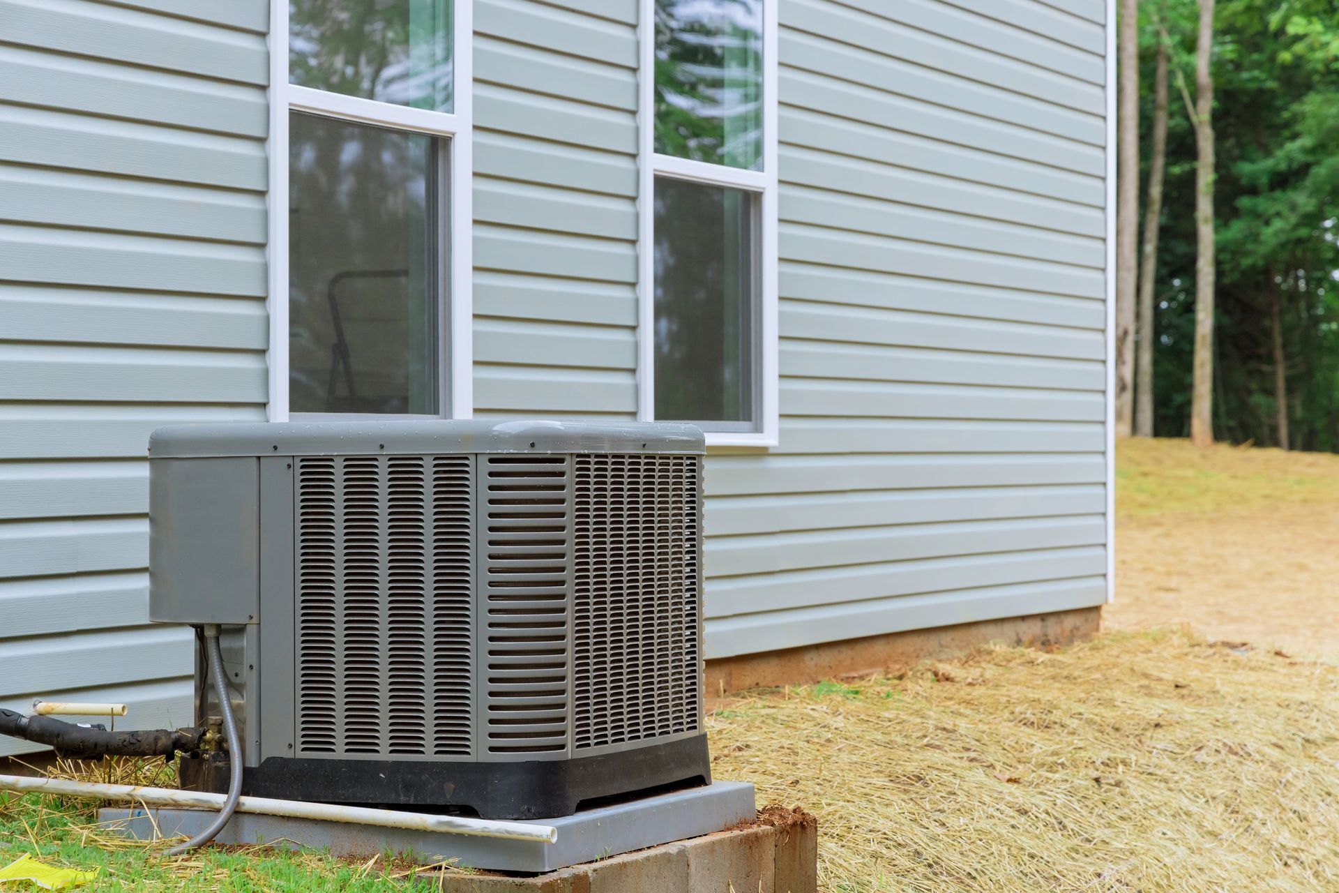 Air conditioning unit outside a building with light blue siding and windows.