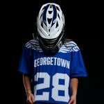 Person in a white helmet and blue Georgetown jersey with number 28, standing against a black background