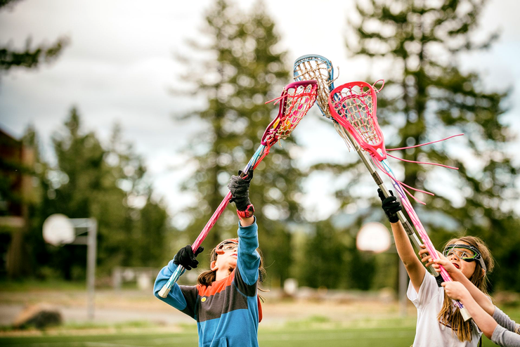 Two lacrosse players raise sticks toward a ball outdoors on a grassy field.