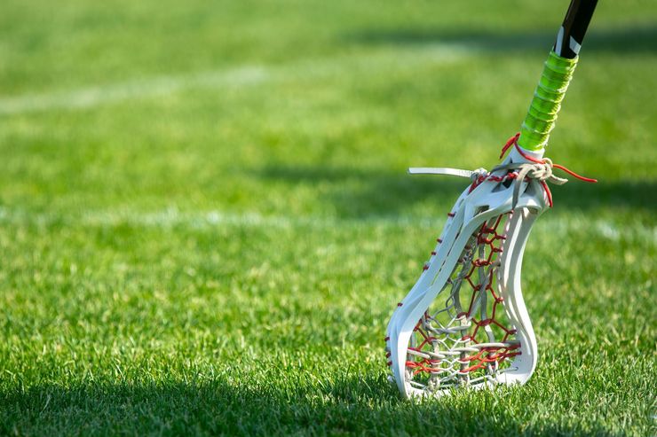 Lacrosse stick with white head and green grip standing on grass field