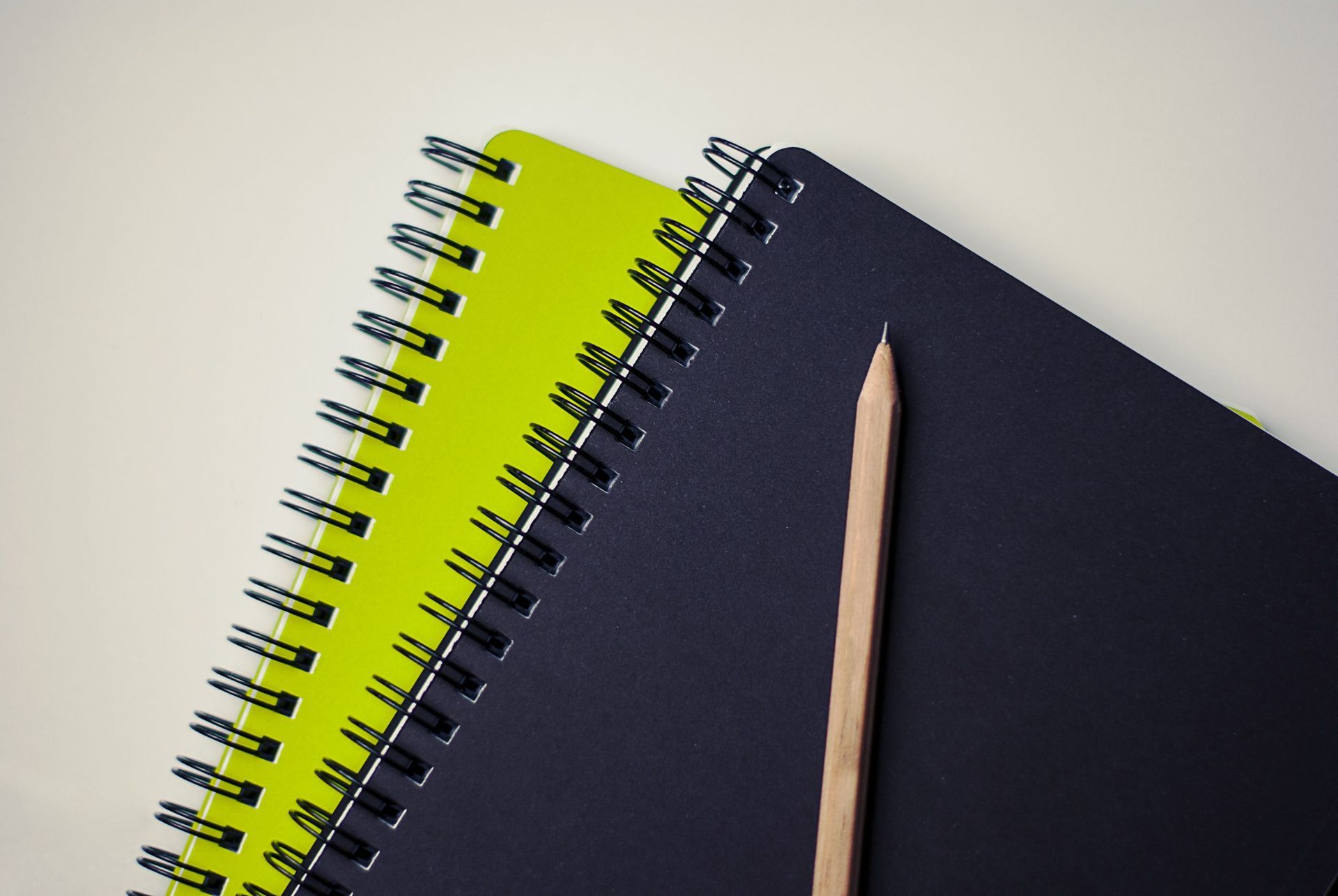 Two spiral notebooks, one neon green and one dark blue, with a wooden pencil on top.