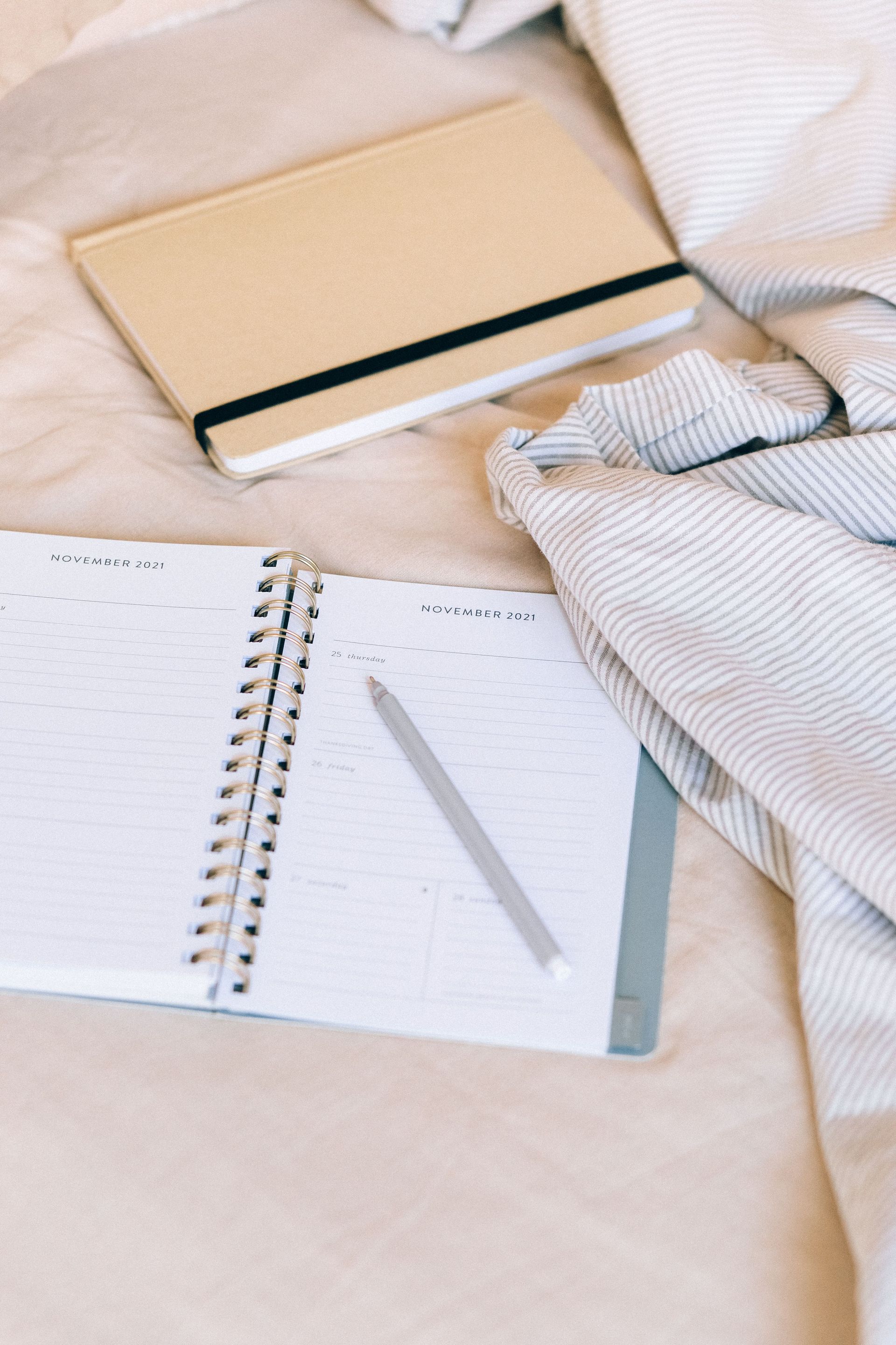 Open notebook with pen on a soft beige bed beside a closed tan journal