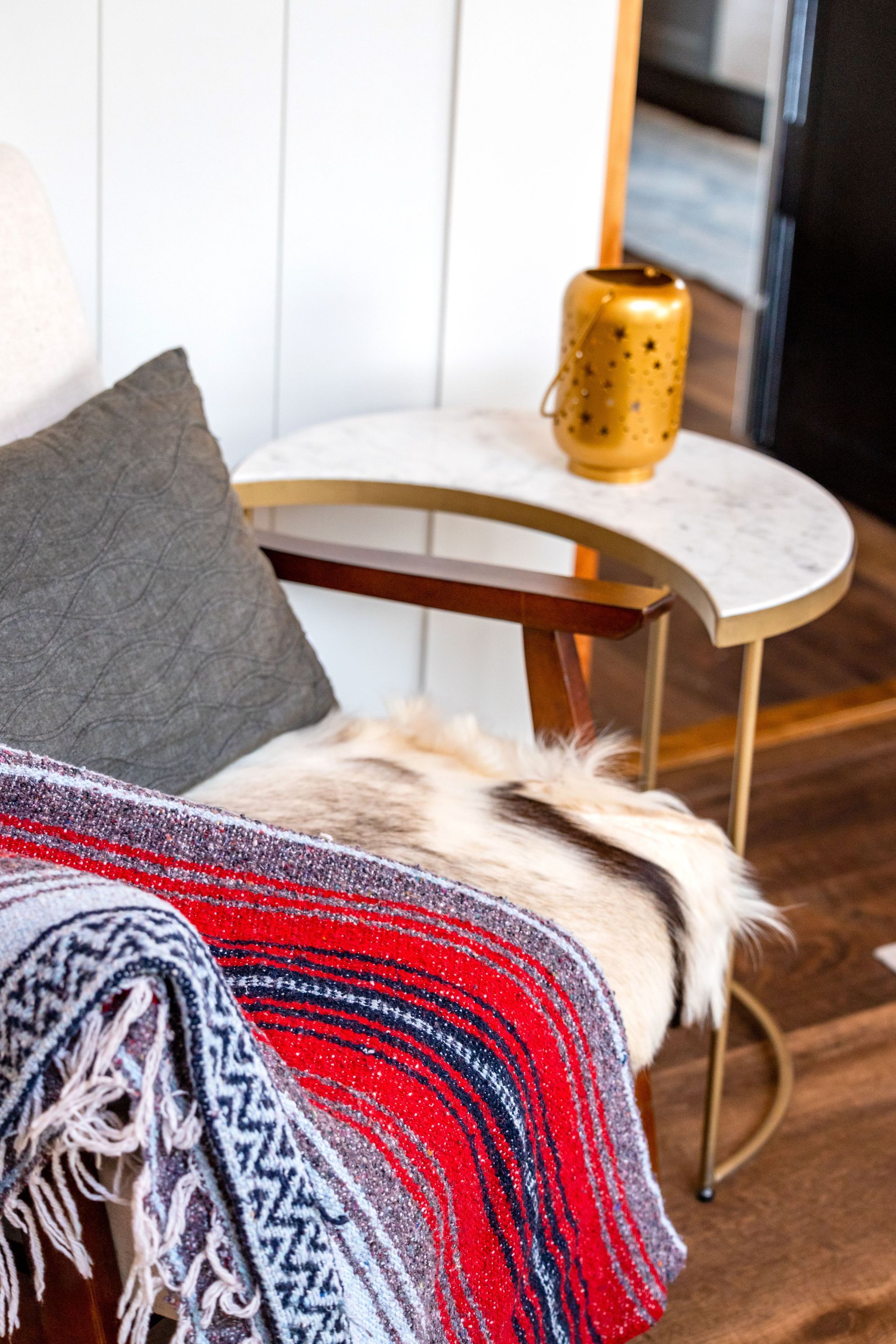 Cozy living room corner with a red blanket, white chair, marble side table, and gold vase.