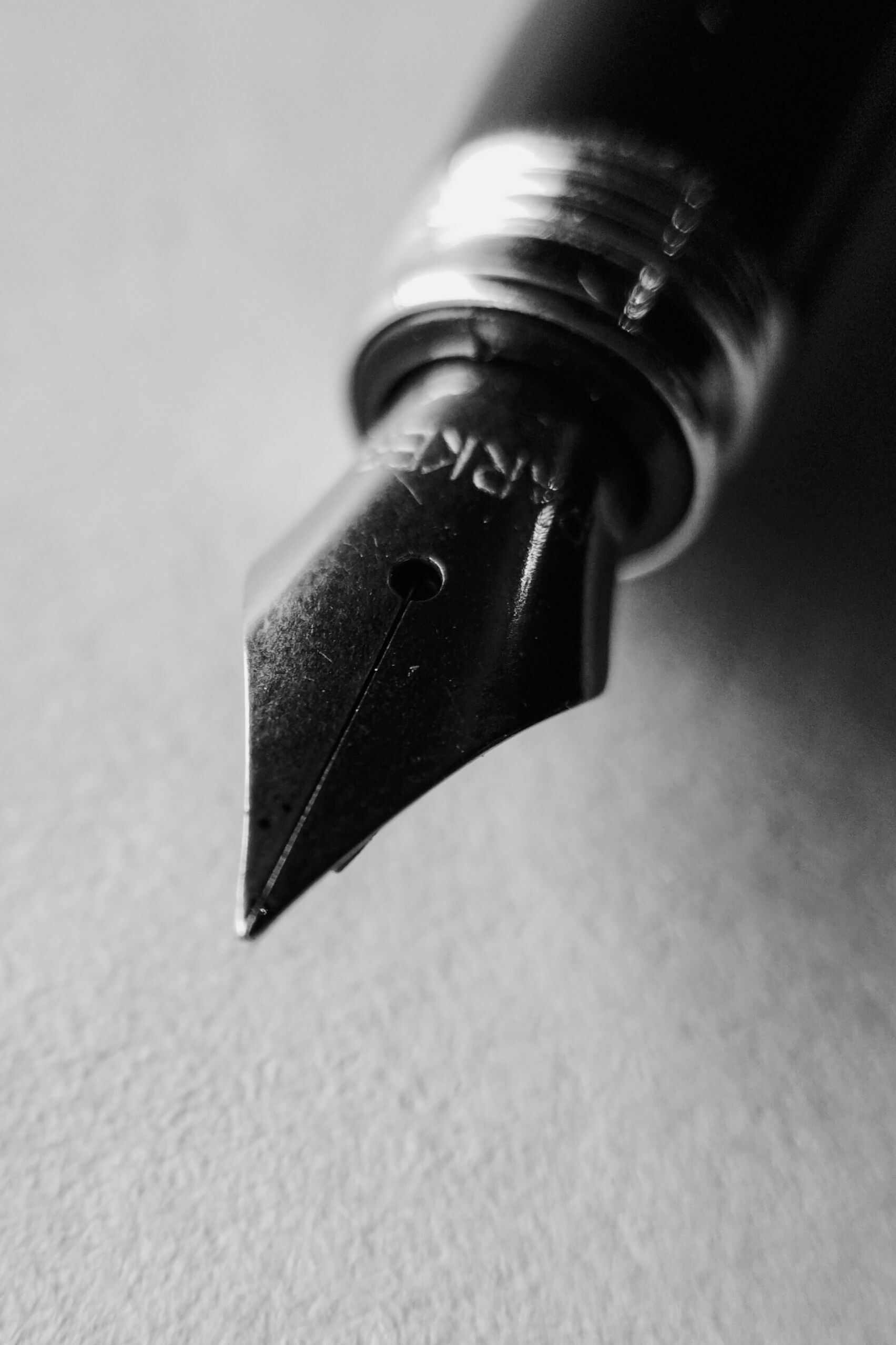Close-up of a fountain pen nib on white paper, in black and silver.