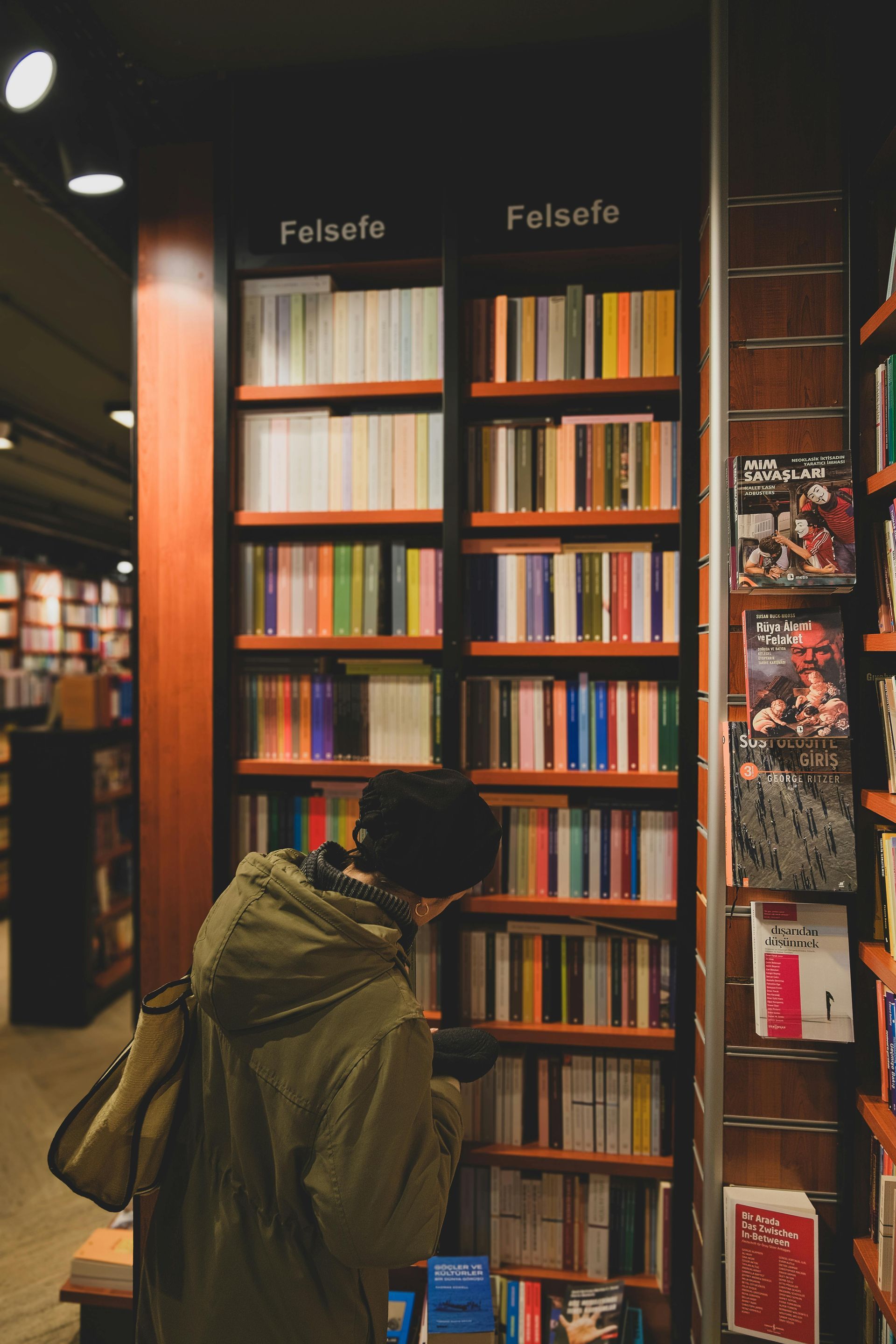 Person browsing colorful books on a wooden bookshelf in a bookstore.