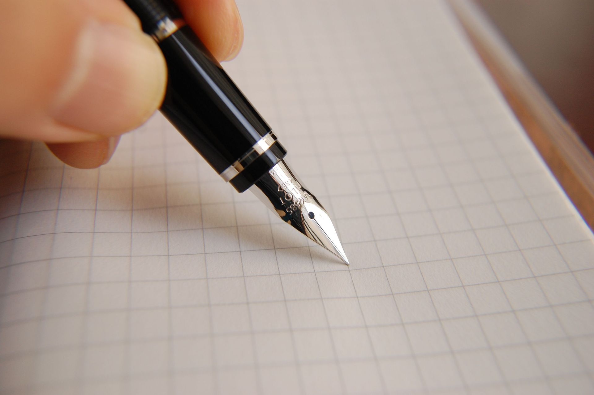Hand holding a black fountain pen poised over lined paper