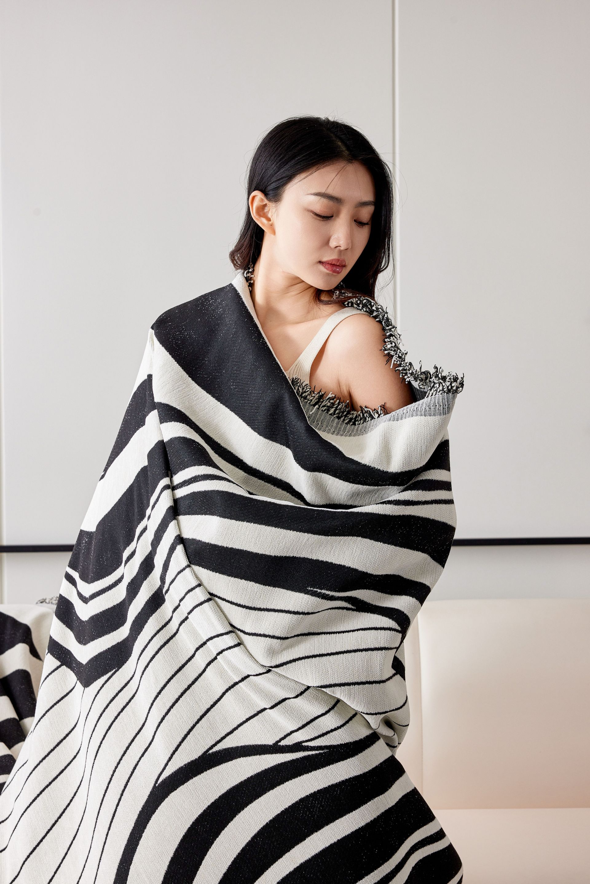 Woman wrapped in a black-and-white striped shawl, looking over her shoulder against a neutral backdrop.