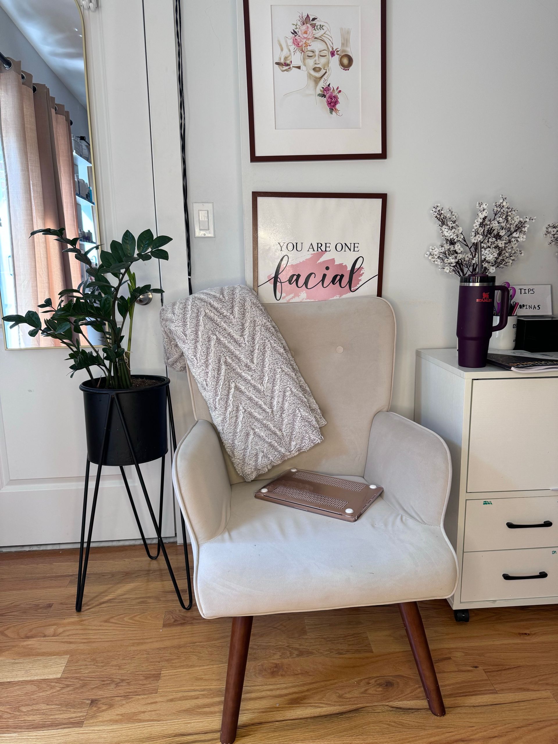 Cozy reading nook with cream armchair, patterned pillow, potted plants, and framed art on a light wall