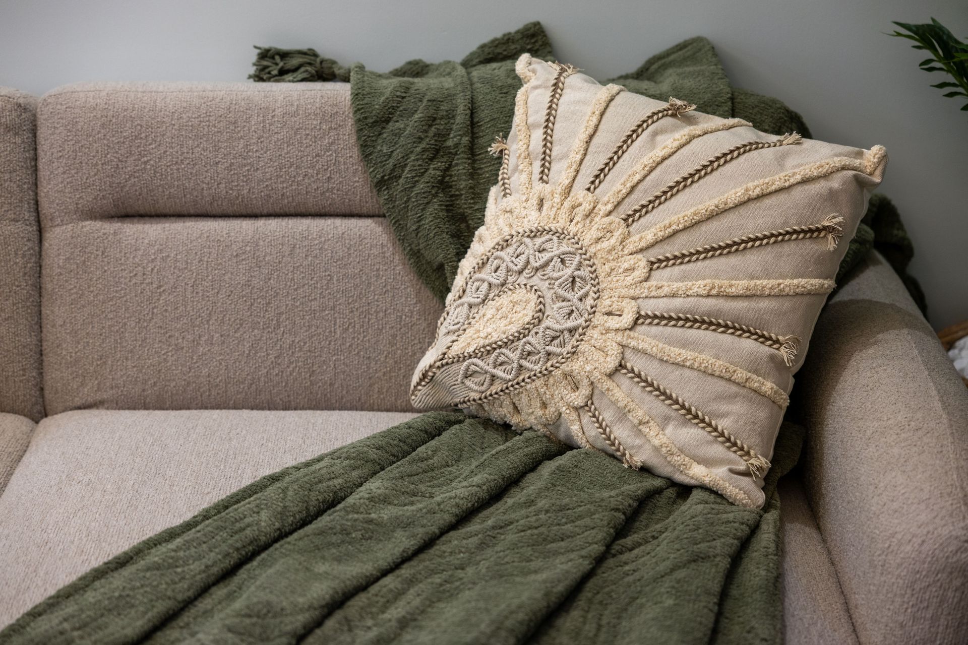 Gray couch with green throw blanket and textured beige decorative pillow