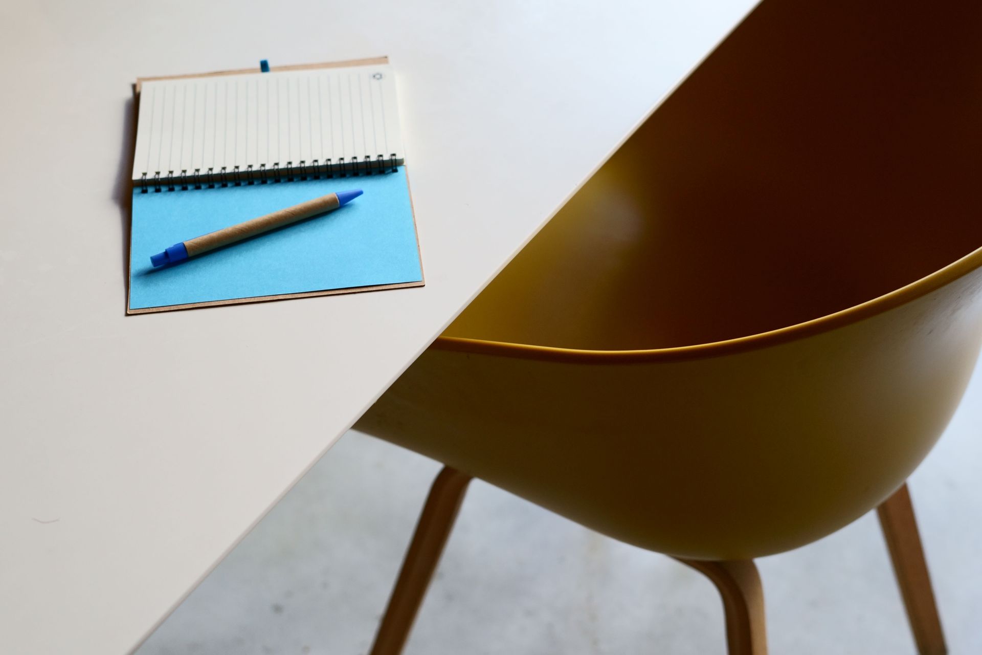 Notepad and pen on a white table beside a brown chair
