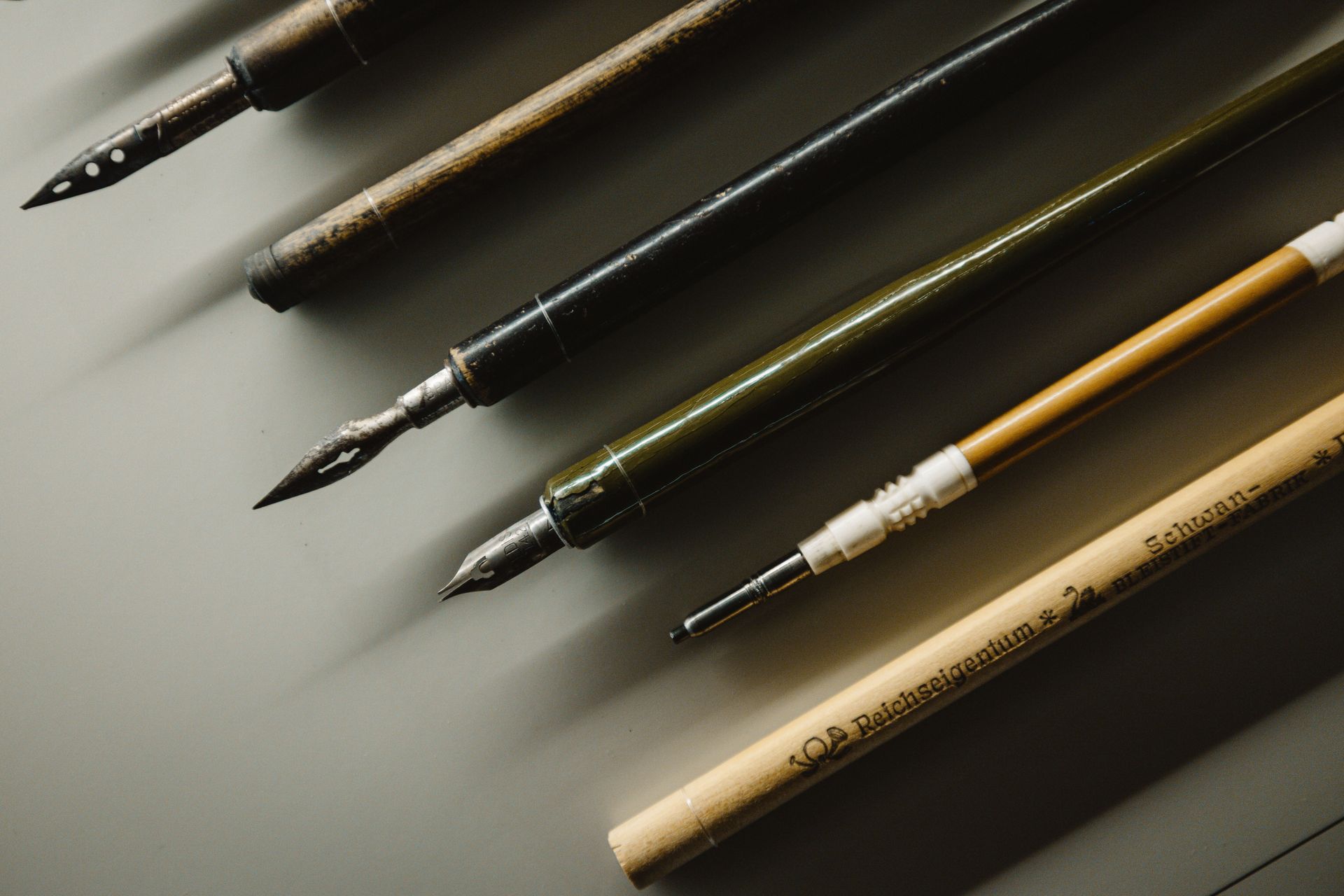 Four paintbrushes and pencils laid diagonally on a gray surface