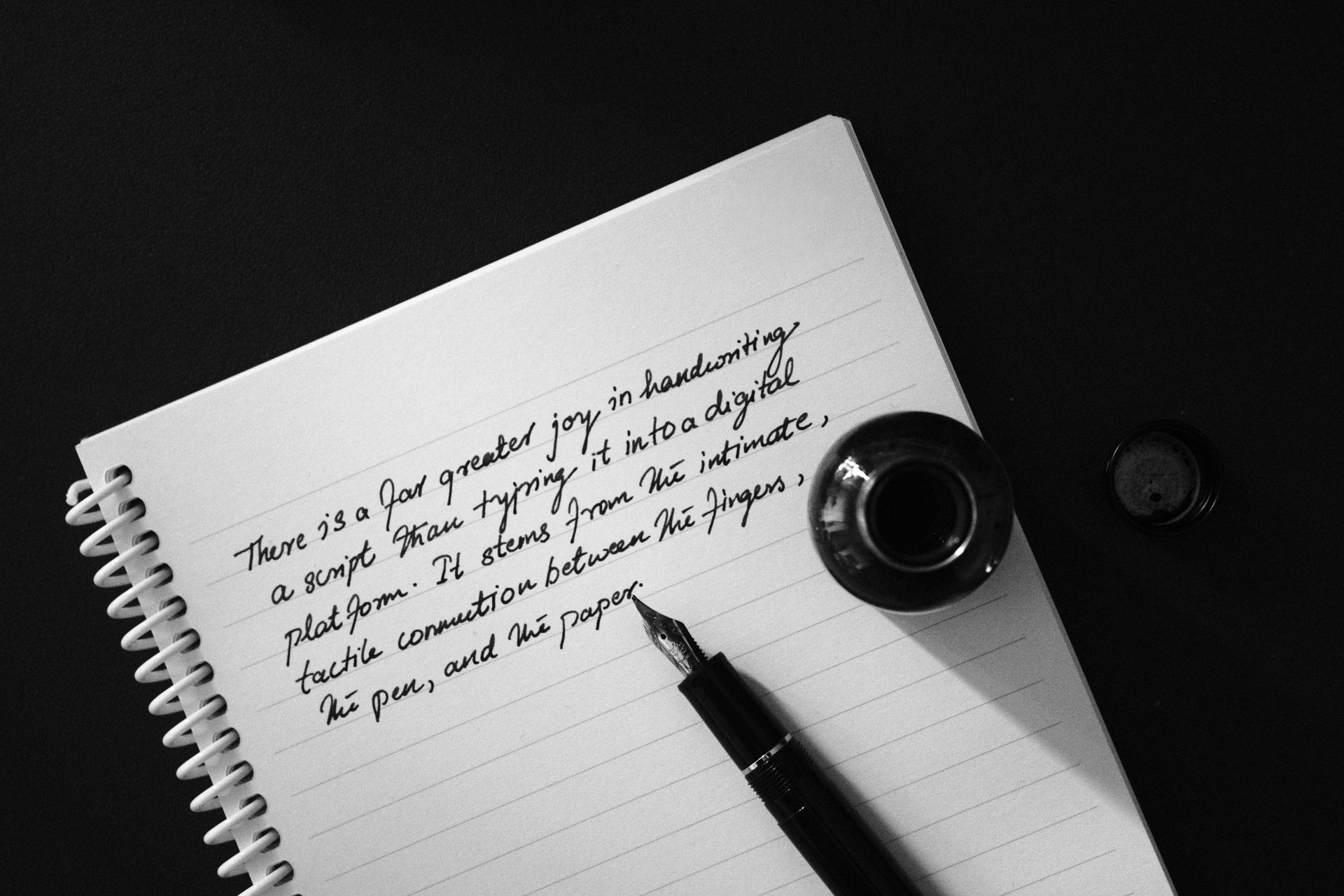 Notebook page with handwritten notes, a fountain pen, and an ink bottle on a dark desk