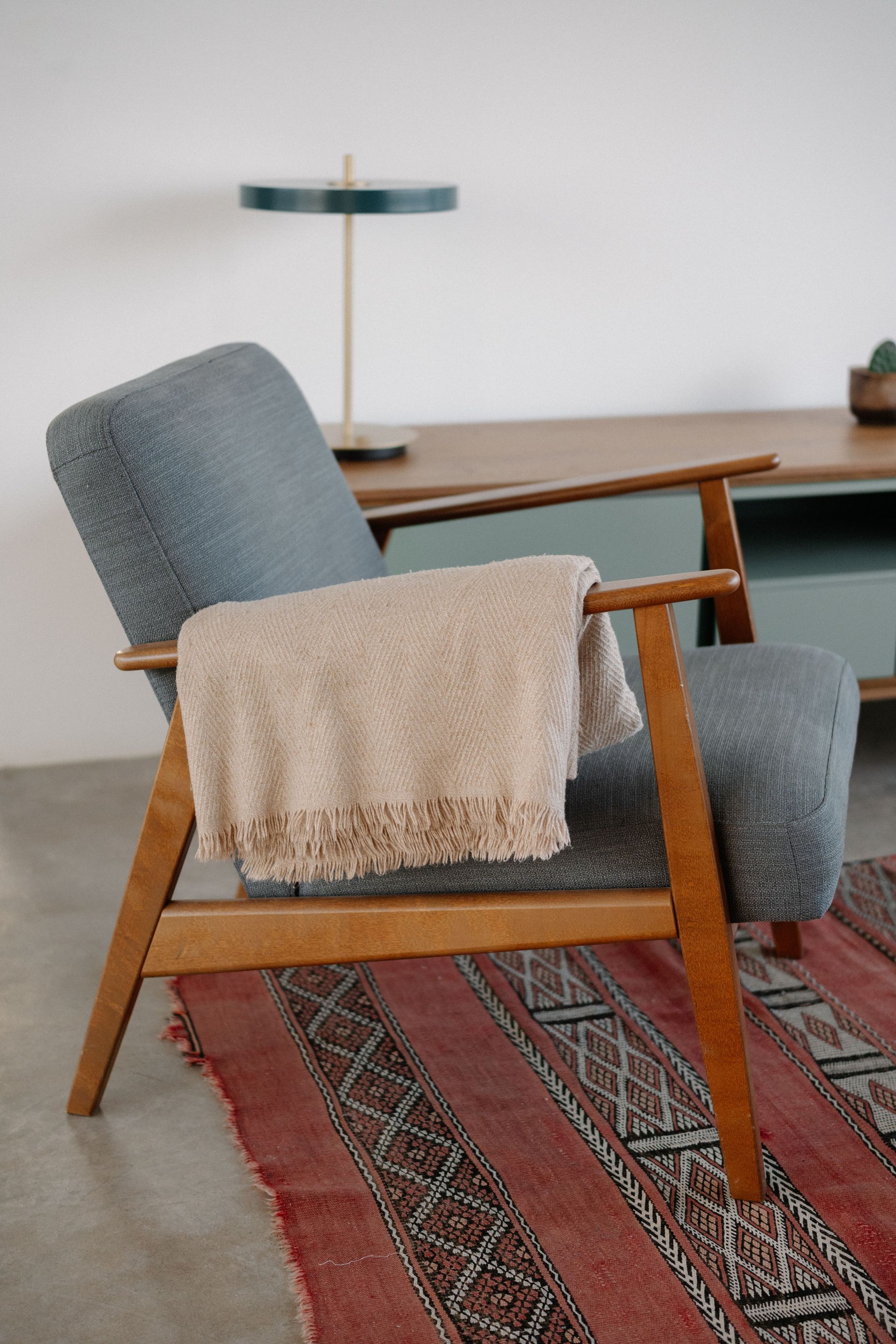 Gray chair with beige throw in a cozy living room beside a wooden desk and patterned rug