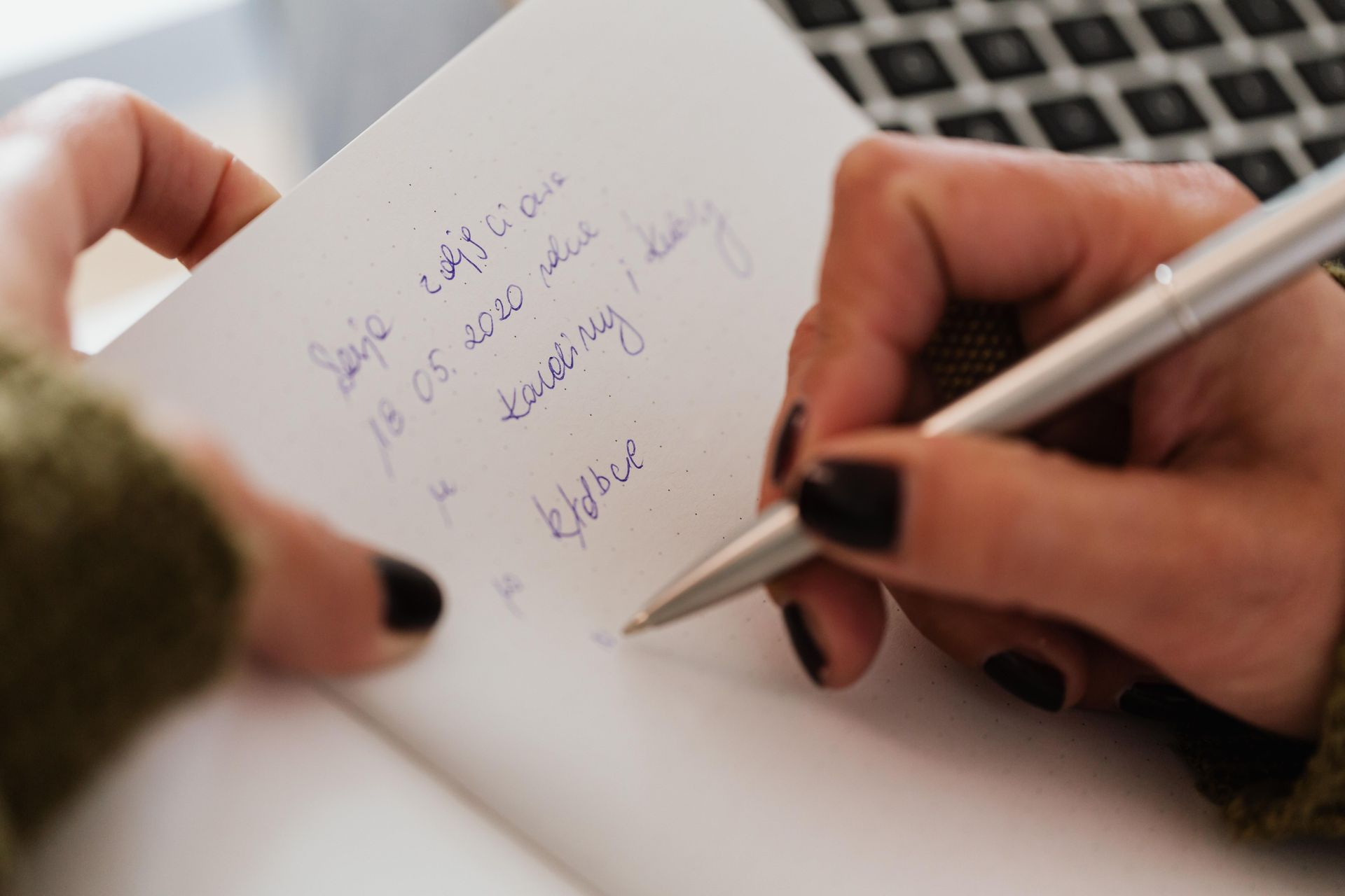Hands writing notes in a notebook with a silver pen.