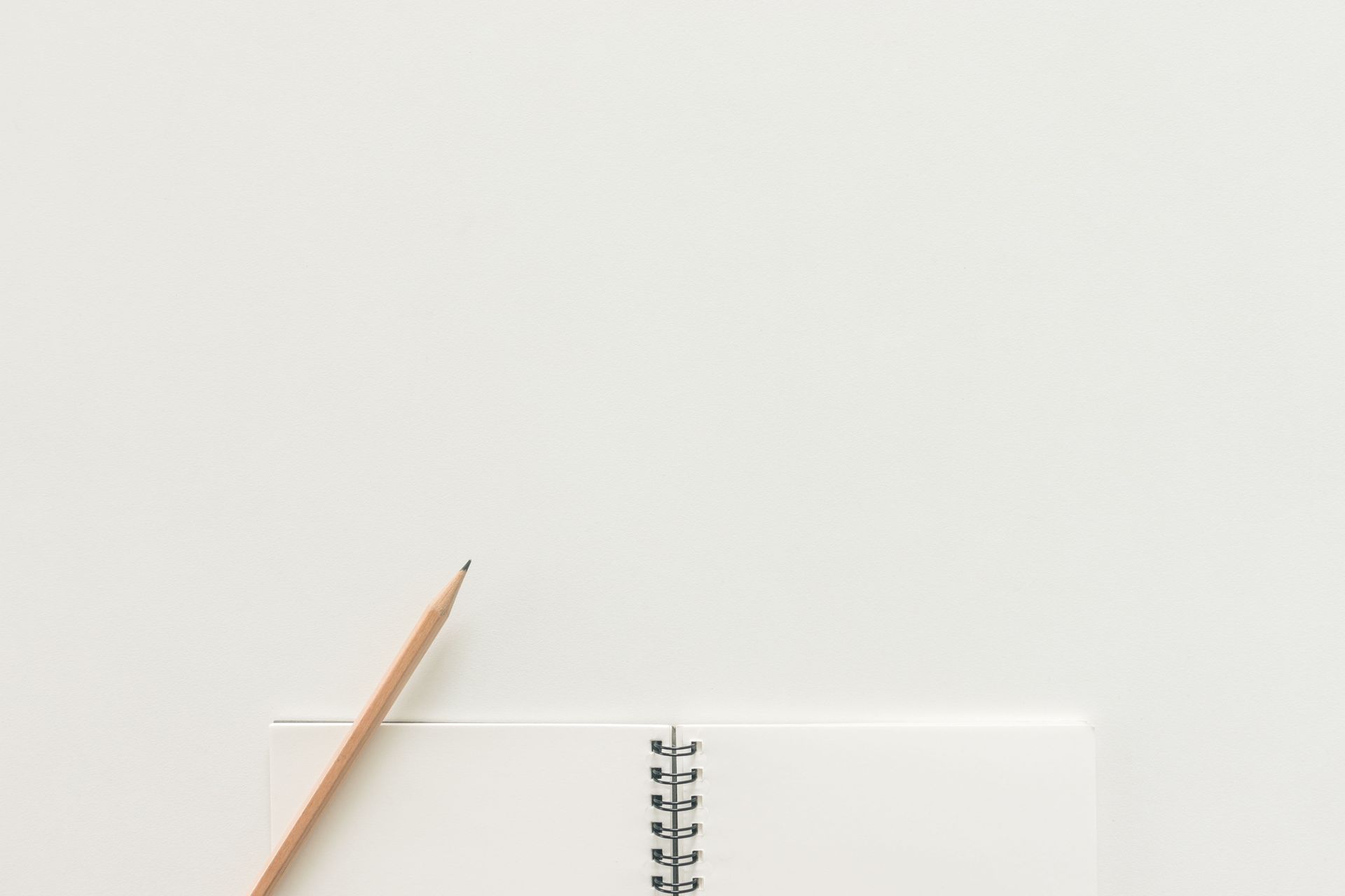 A pencil beside a spiral notebook on a white desk