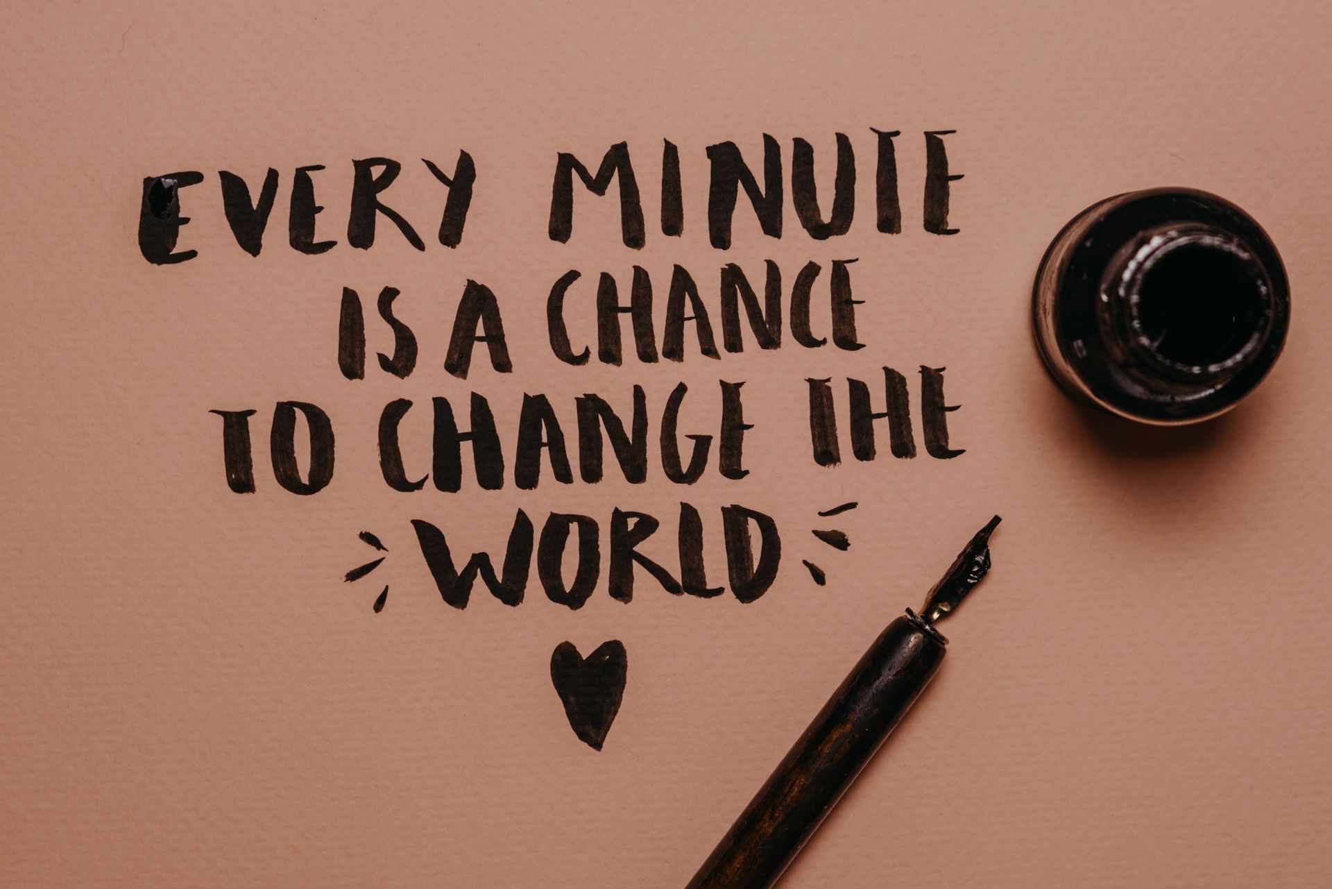Hand-lettered quote on pink paper: “Every minute is a chance to change the world,” with pen and ink jar.