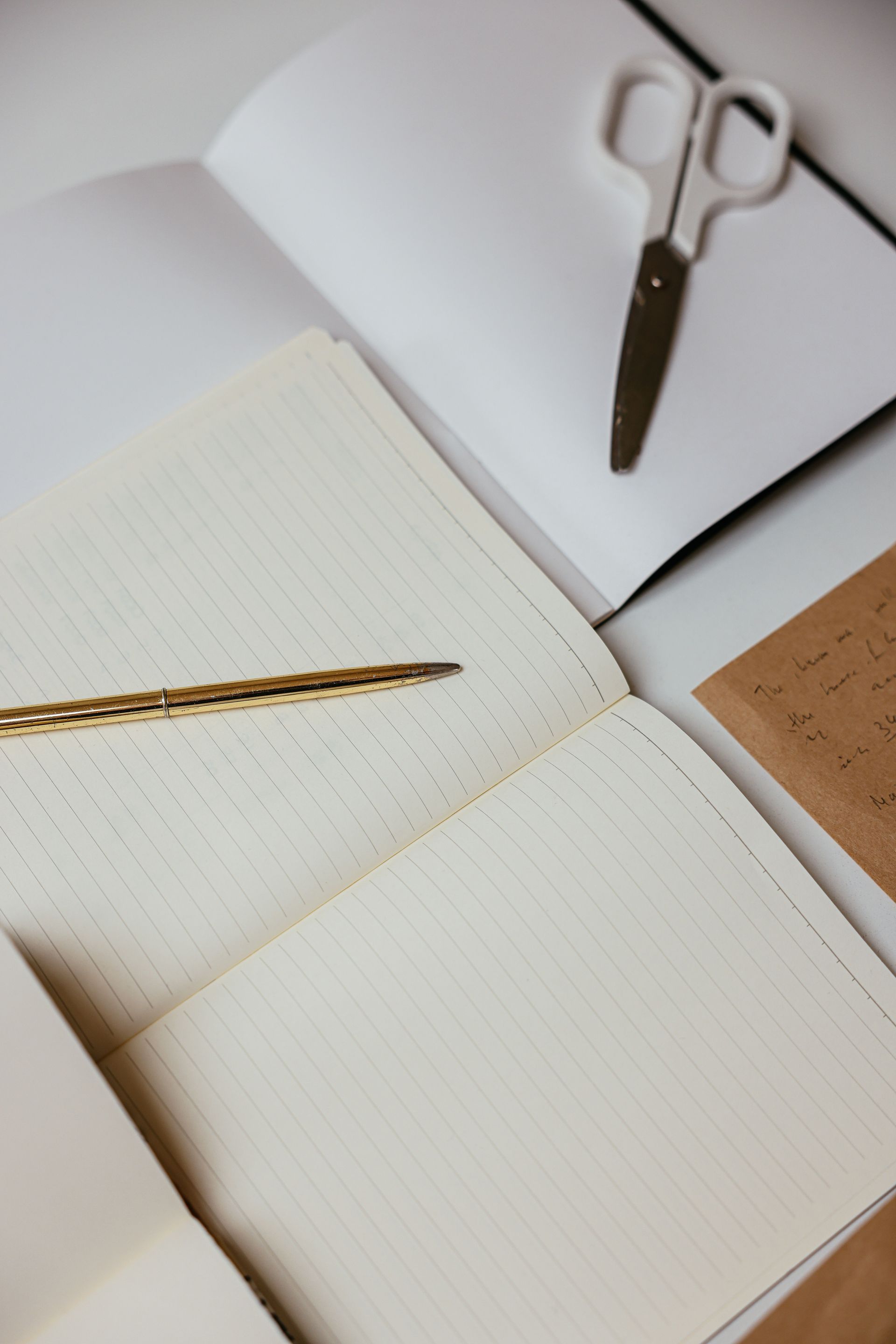 Open notebook with gold pen beside scissors and white paper on a desk