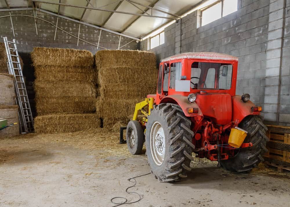 A Red Tractor Is Parked in A Barn Filled with Hay Bales — Thompson's Farm Gear In Wauchope, NSW