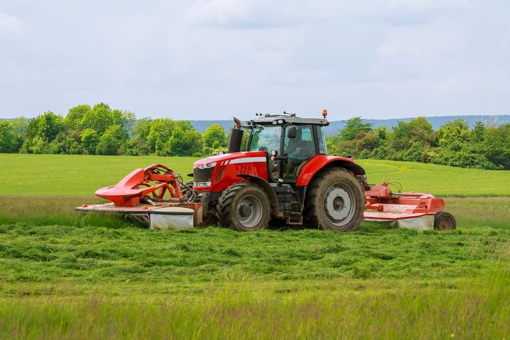 A Red Tractor Is Cutting Grass in A Field — Thompson's Farm Gear In Wingham, NSW