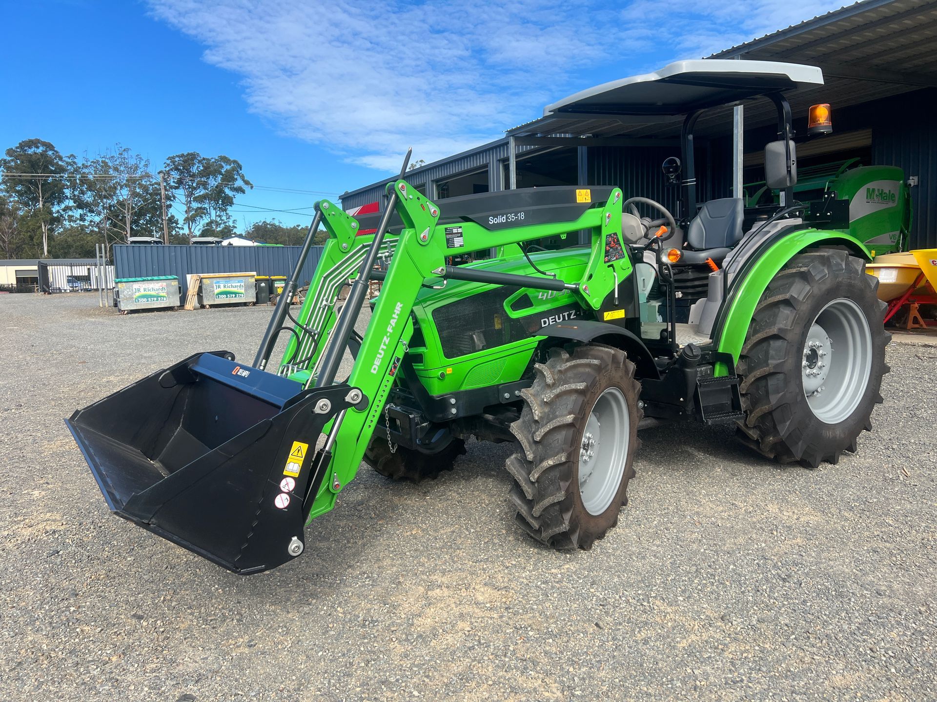 A Green Tractor with A Black Bucket Is Parked in A Gravel Lot — Thompson's Farm Gear In Wauchope, NSW