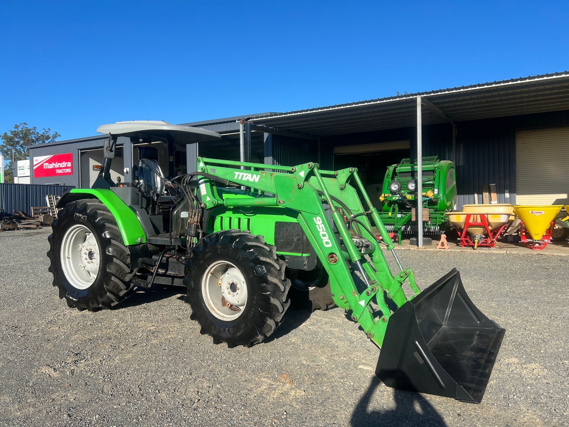 A green tractor with a black bucket is parked in front of a building — Thompson's Farm Gear In Wauchope, NSW