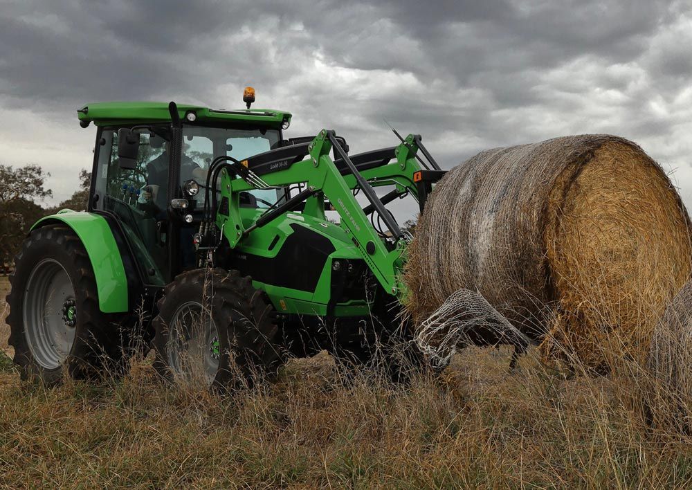Green Tractor Lifting a Hay Bale — Thompson's Farm Gear In Wauchope, NSW
