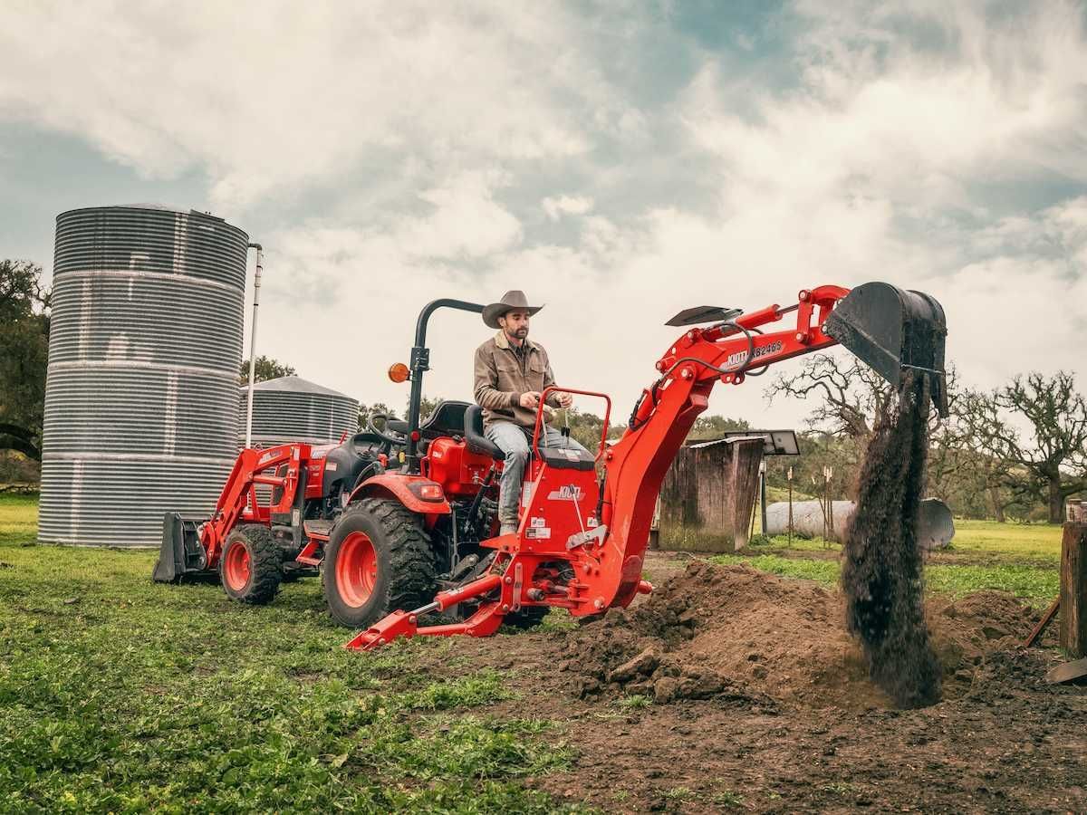 Farmer Operating A Red Tractor Front Loader, Spreading Soil In A Field — Thompson's Farm Gear In Kempsey, NSW