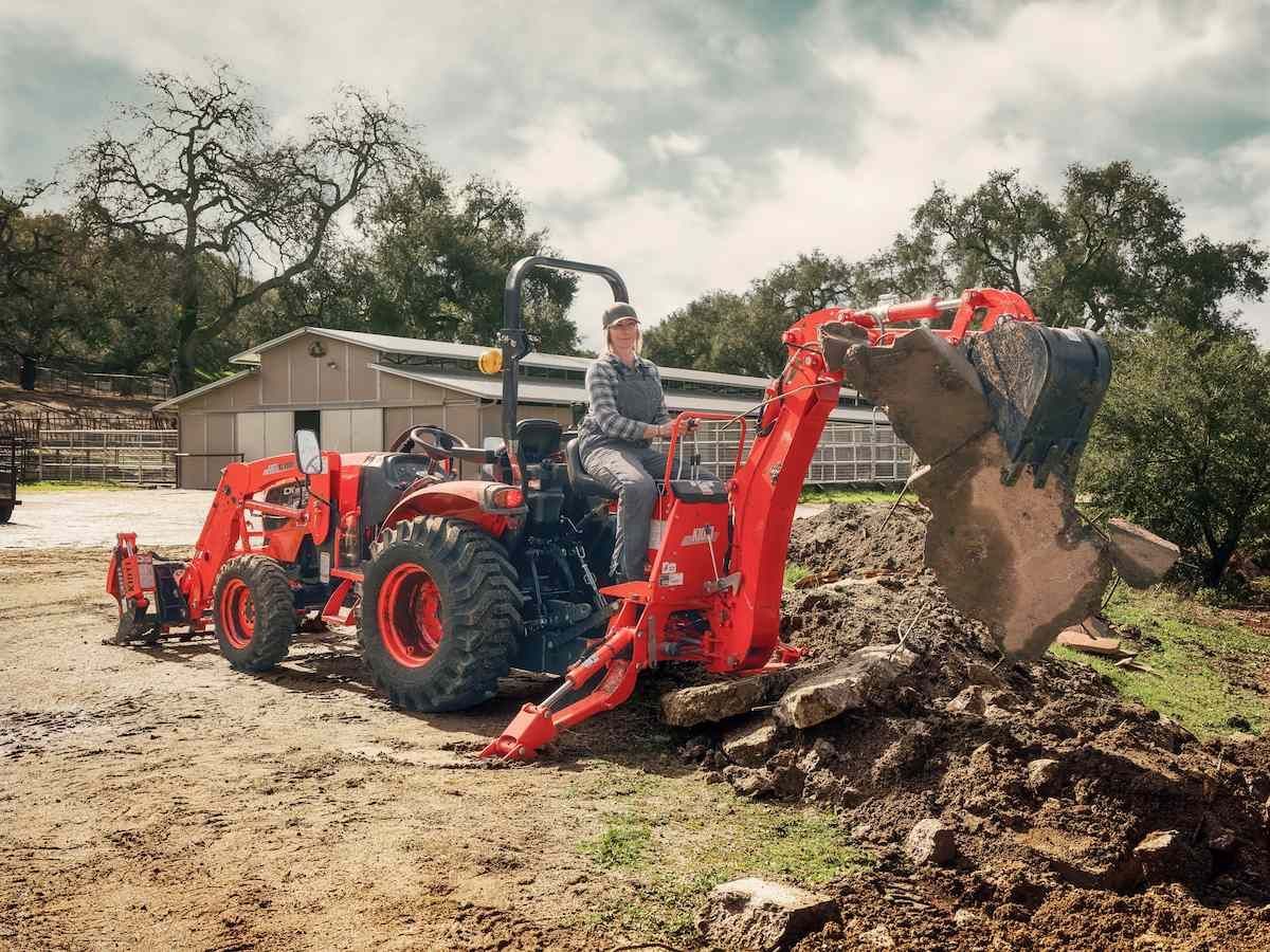 Orange Tractor Digging Dirt With Backhoe In A Muddy Yard — Thompson's Farm Gear In Coffs Harbour, NSW