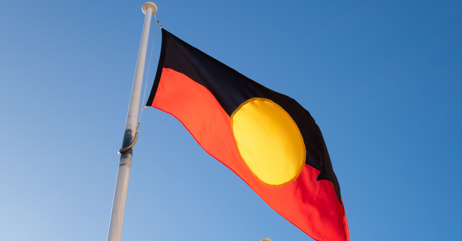Australian Aboriginal flag flying against a blue sky