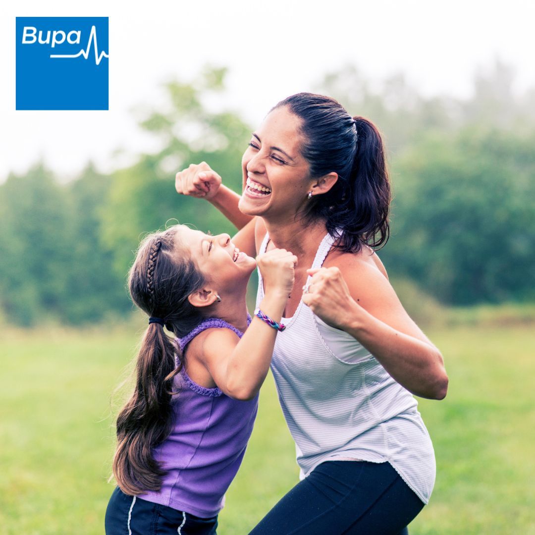 A woman and child are playing in a field with a bupa logo in the background