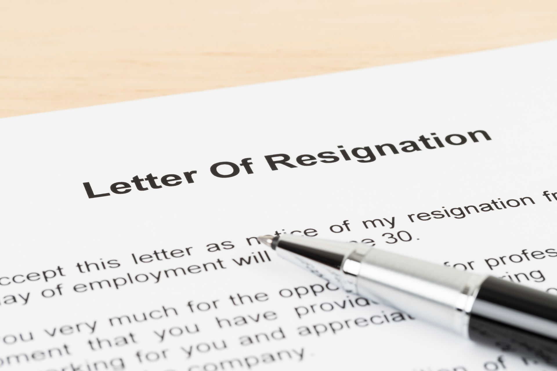 Close-up of a resignation letter with a pen, ready to be signed, on a wooden surface.