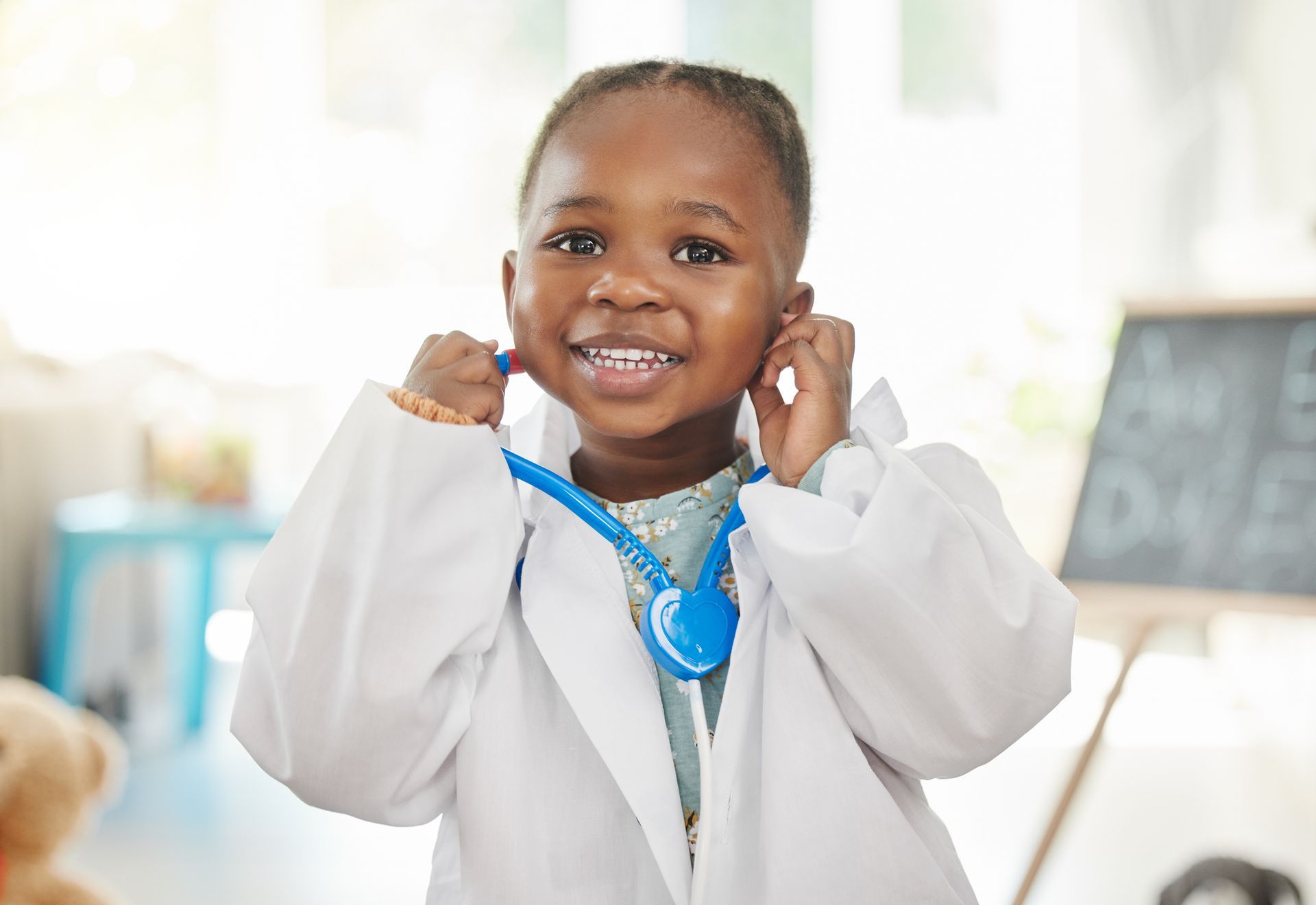 A little girl is wearing a lab coat and holding a stethoscope around her neck.