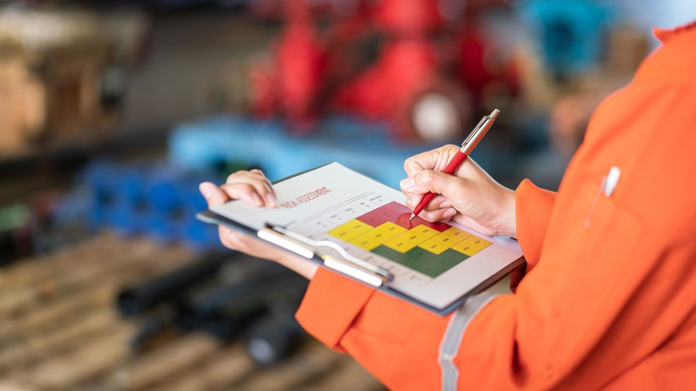 Person in orange coveralls writing on clipboard with bar graph in industrial setting.