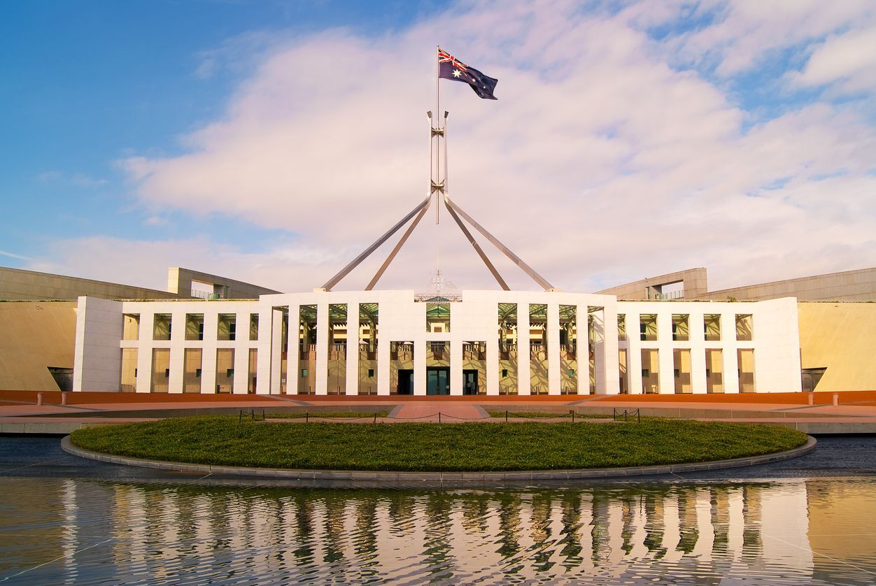 Australian Parliament House with flag flying; blue sky, reflection in water.