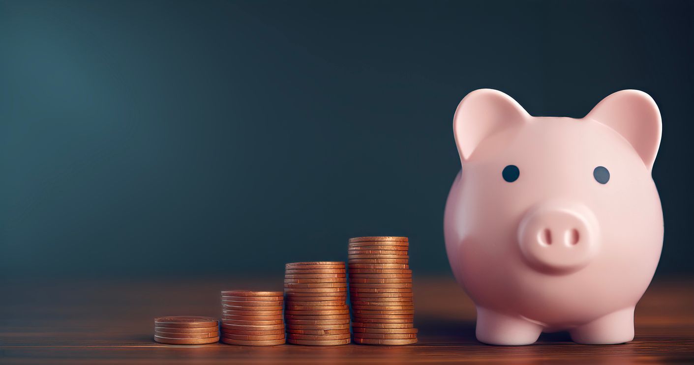 A pink piggy bank sits next to four staggered stacks of gold coins against a dark, moody background.