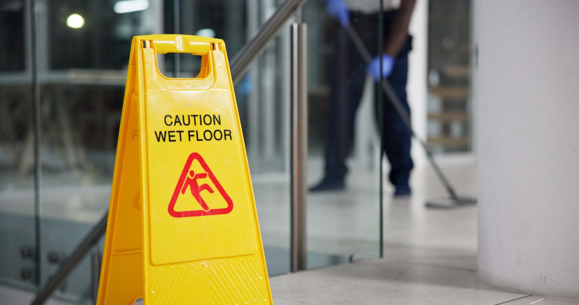 A man is mopping the floor next to a yellow caution wet floor sign.