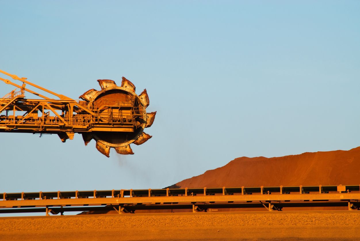 Large mining machine, orange and yellow, extracting material near a brown mountain, blue sky backdrop.